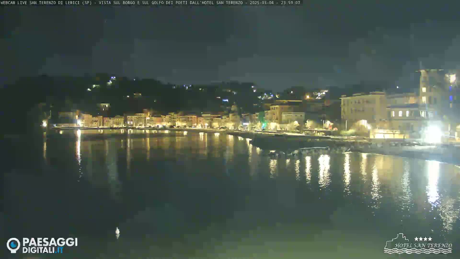 A nighttime view of a waterfront town with lights reflecting on calm water.