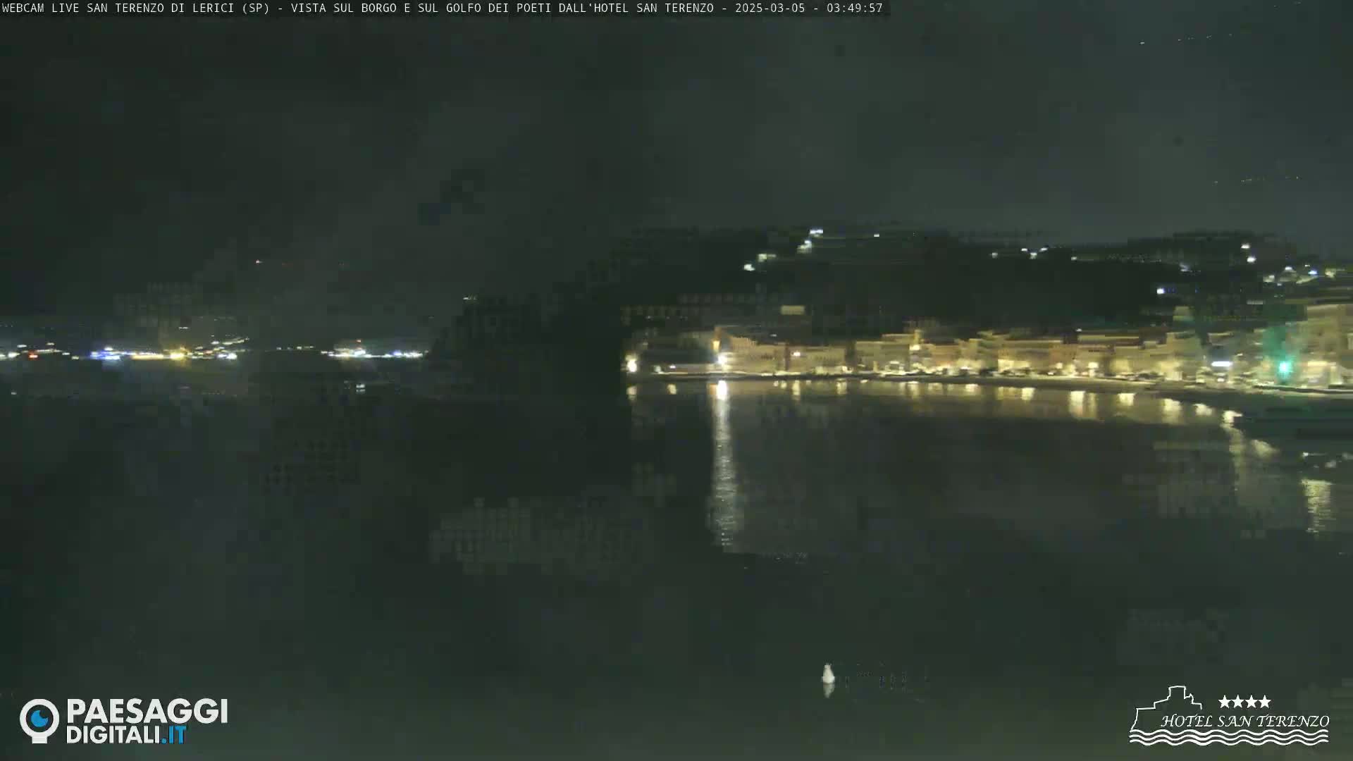 A nighttime view of a town's waterfront, illuminated by lights reflecting on the calm water.