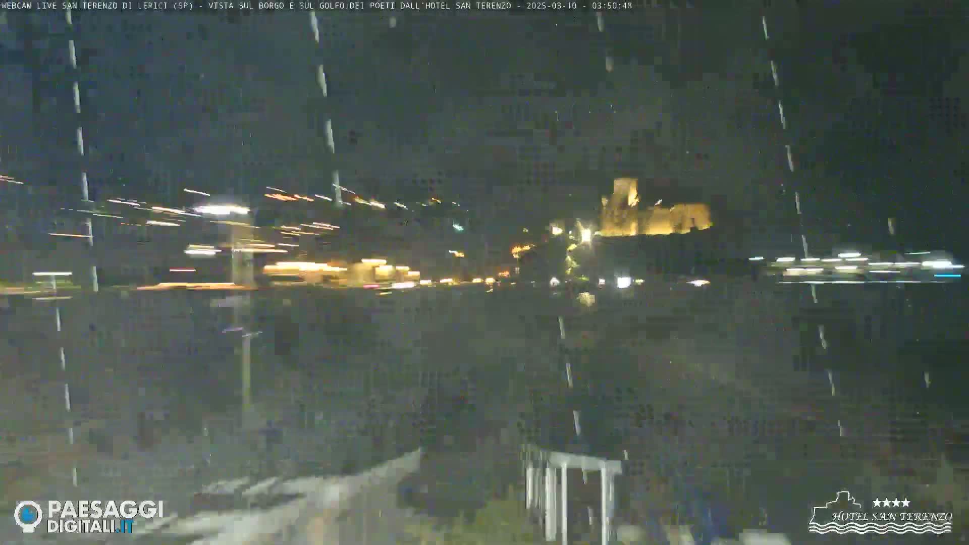 A nighttime, snowy view of a town with lights from vehicles and buildings, showing light streaks from moving cars.
