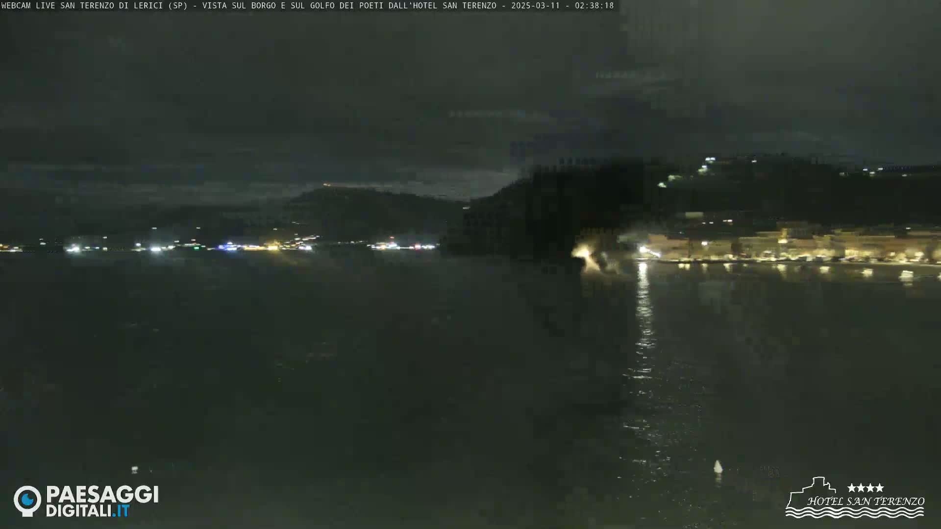 A nighttime view across a dark body of water shows a dimly lit shoreline with buildings and faint lights.