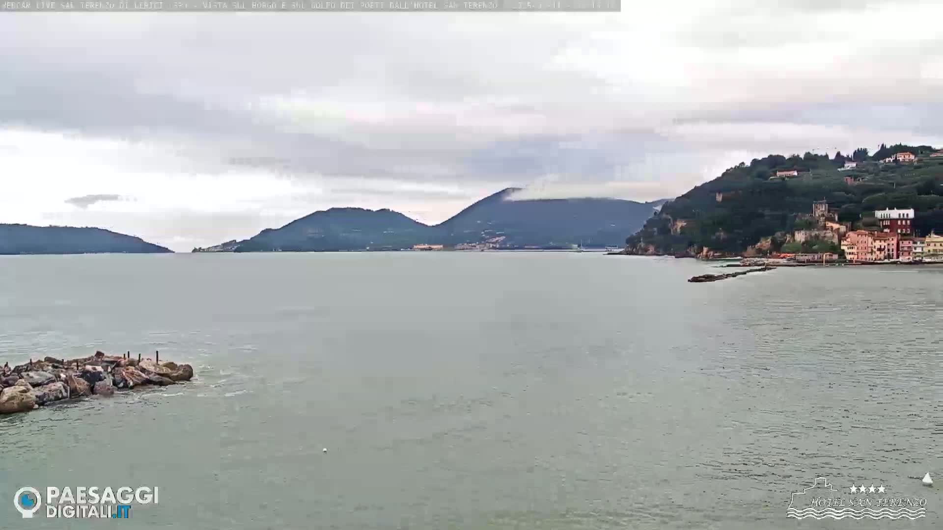 A calm, overcast day reveals a coastal town nestled beside a body of water, backed by rolling green hills.