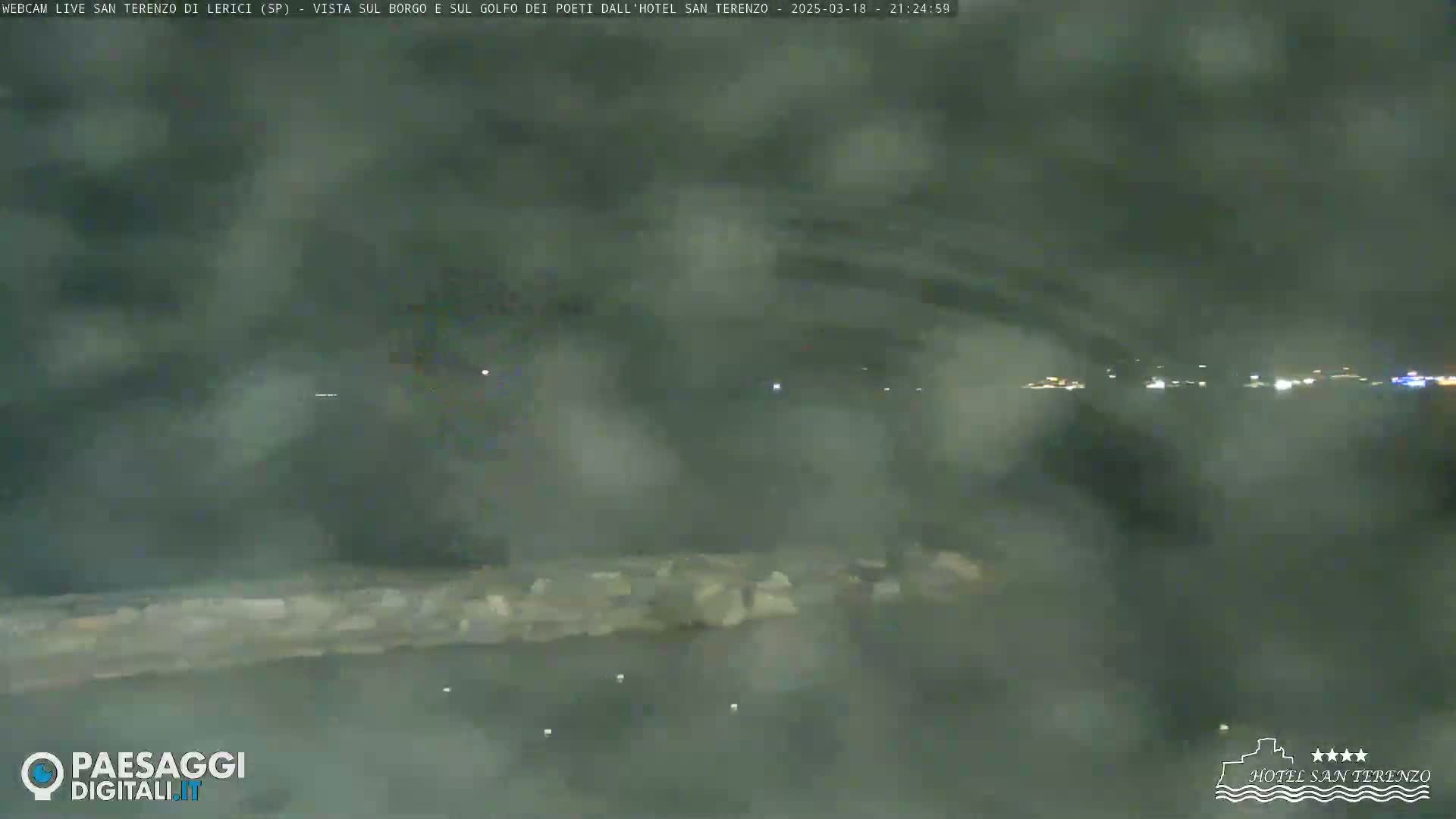A nighttime view of a body of water with a low-lying wall or structure in the foreground, under hazy or foggy conditions.