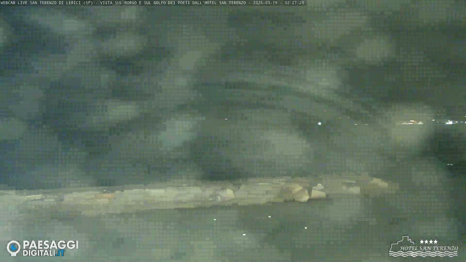 A nighttime view of a rocky shoreline and a hazy, dark body of water under a cloudy sky.