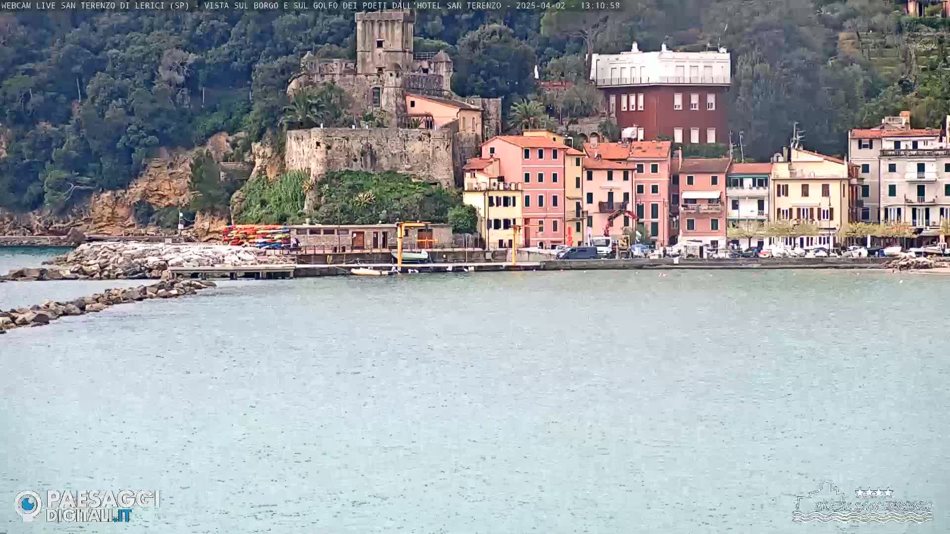 A coastal town with colorful buildings, a stone castle, and a calm sea under an overcast sky.