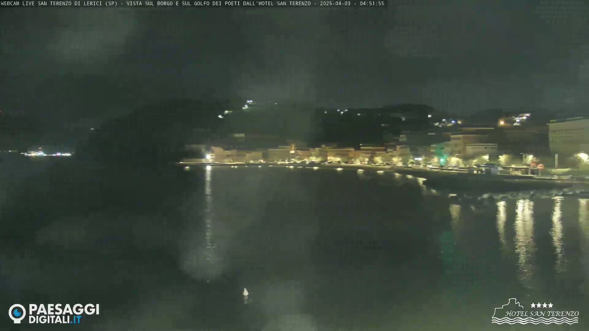 A nighttime view of a calm body of water reflecting the lights of a town on the opposite shore.