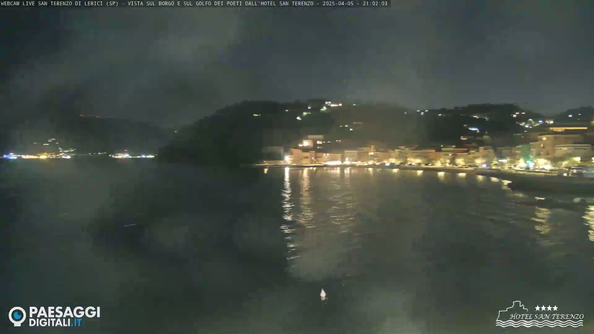 A nighttime view of a coastal town with lights reflecting on calm water.