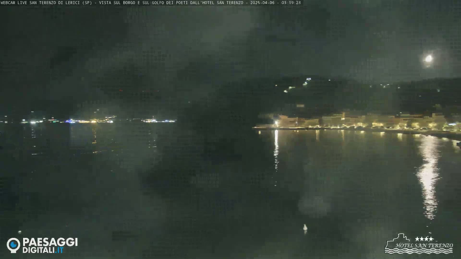 A nighttime view of a calm body of water reflecting lights from buildings on the shore under a mostly clear night sky.