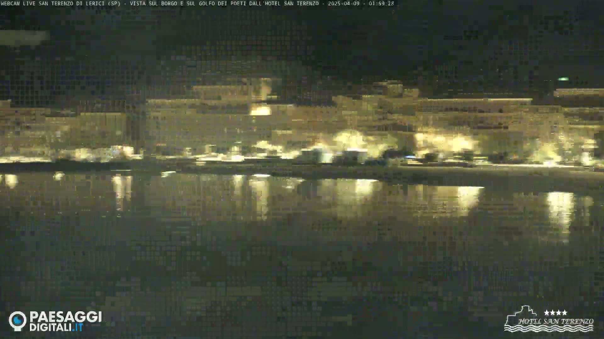 A nighttime view of a town's lights reflected in calm water.