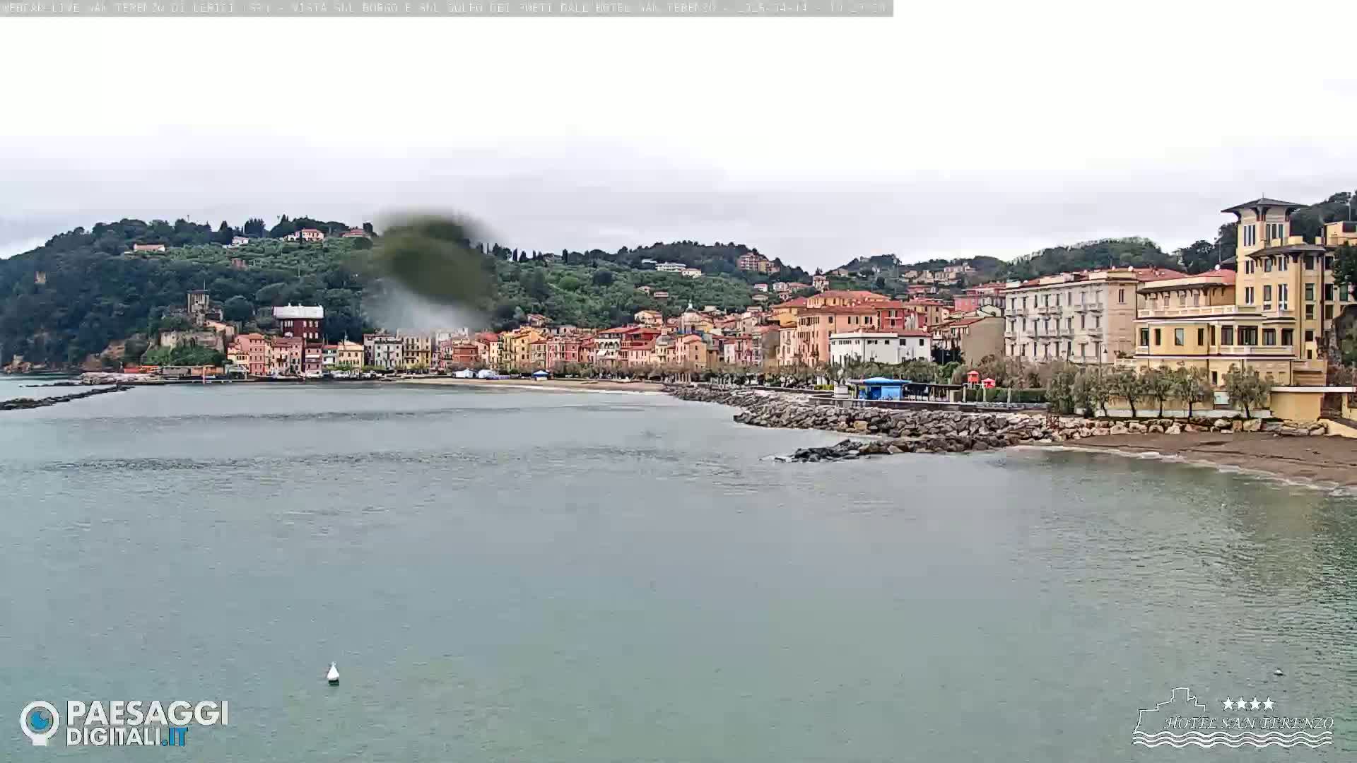 A seaside town with multi-story buildings, a sandy beach, and a calm body of water under an overcast sky.