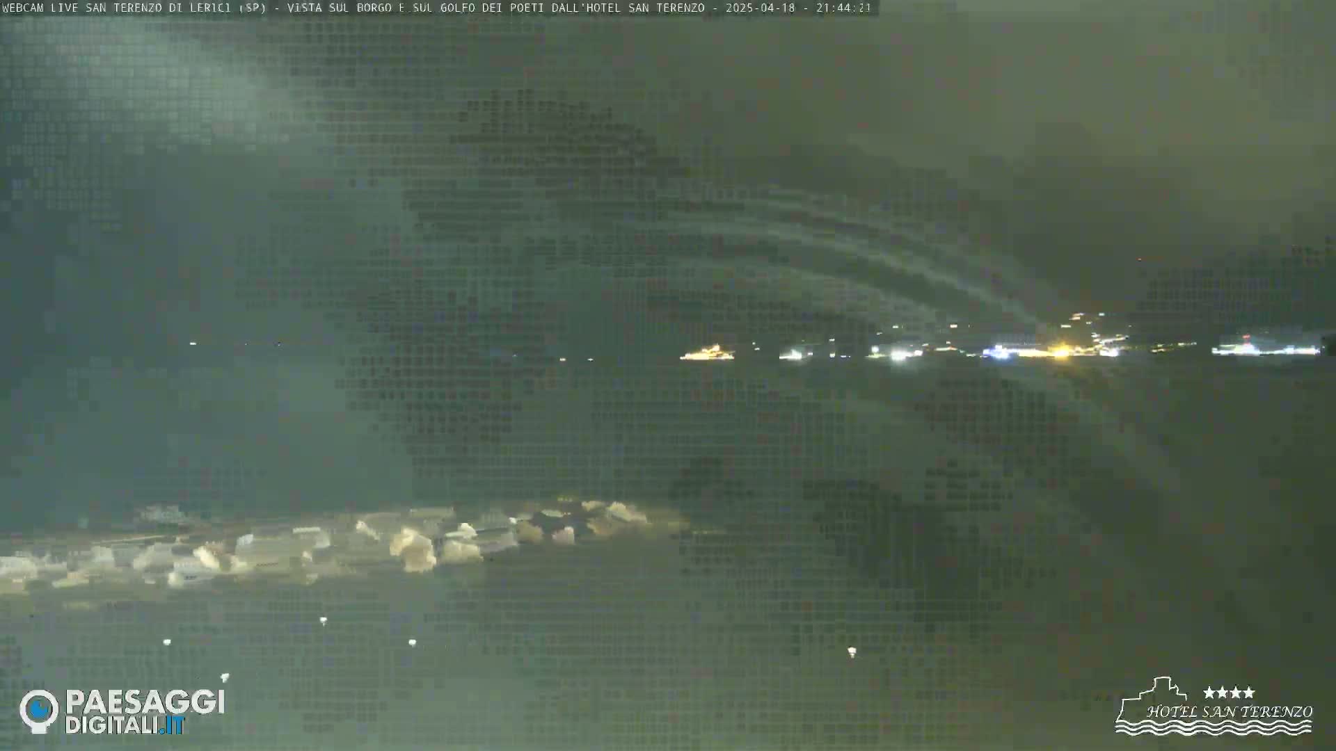 A nighttime, blurry long shot of a body of water with lights visible on the far shore under an overcast sky.