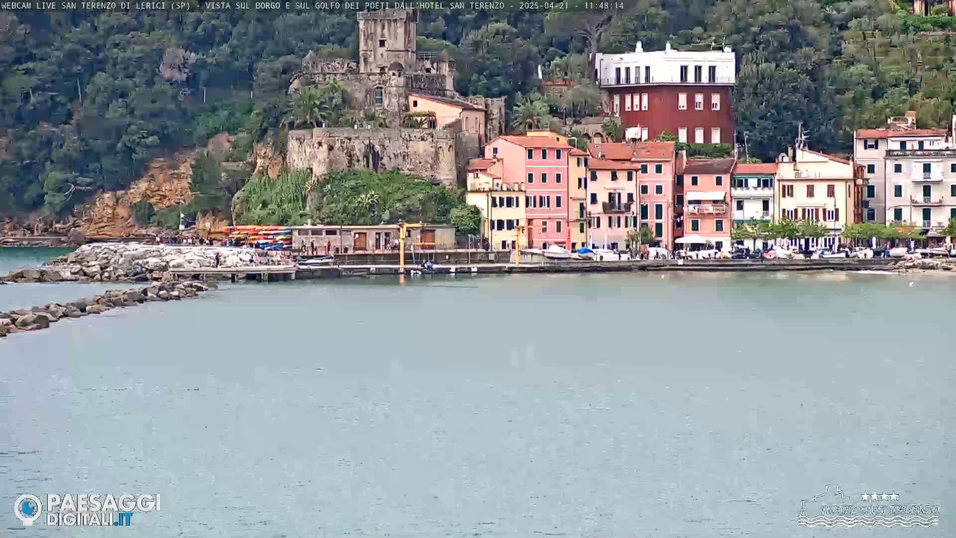 A waterfront village with colorful buildings and a stone pier sits on a calm sea under an overcast sky.