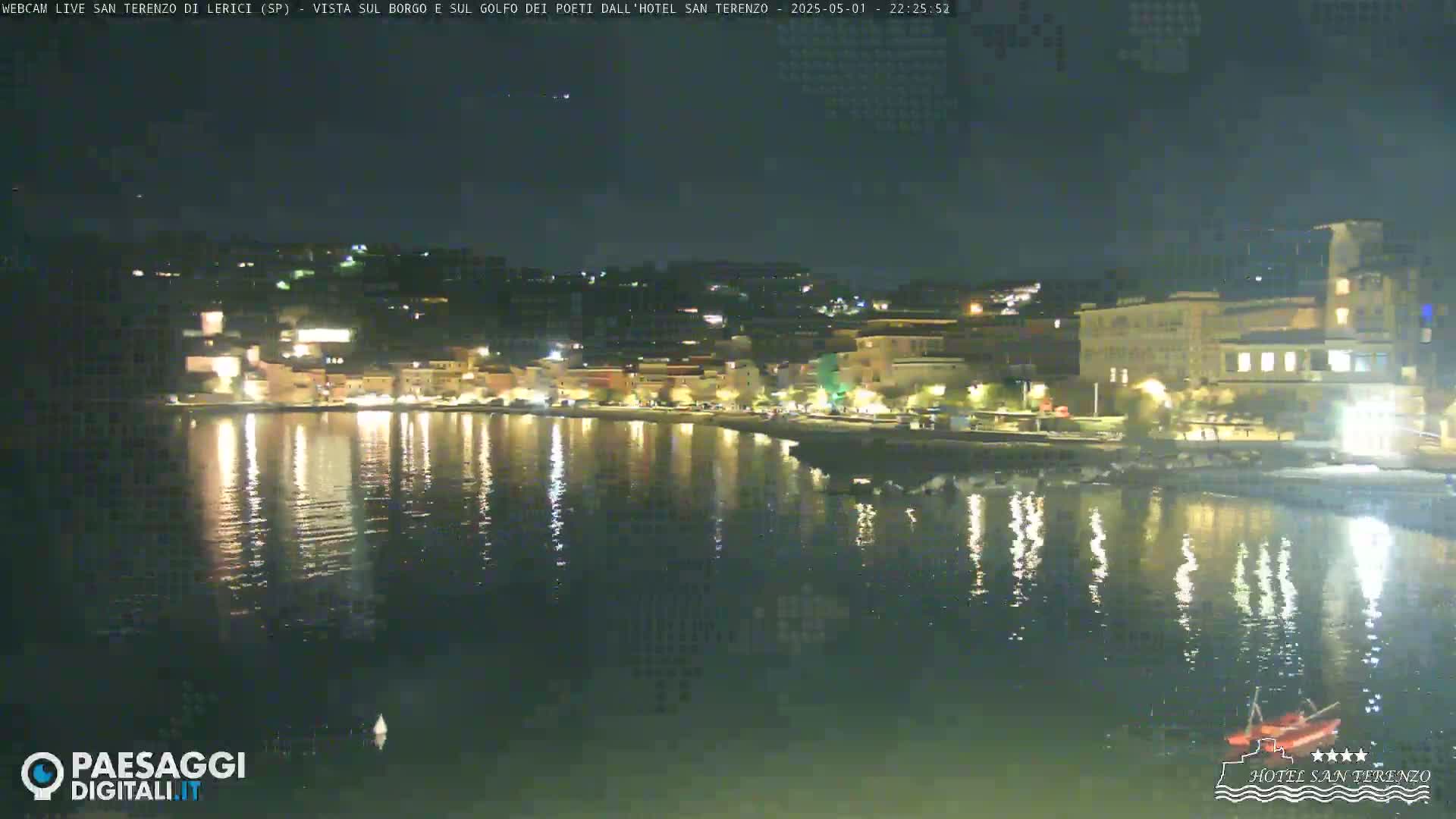 A nighttime view of a calm body of water reflecting the lights of a town on the shore.