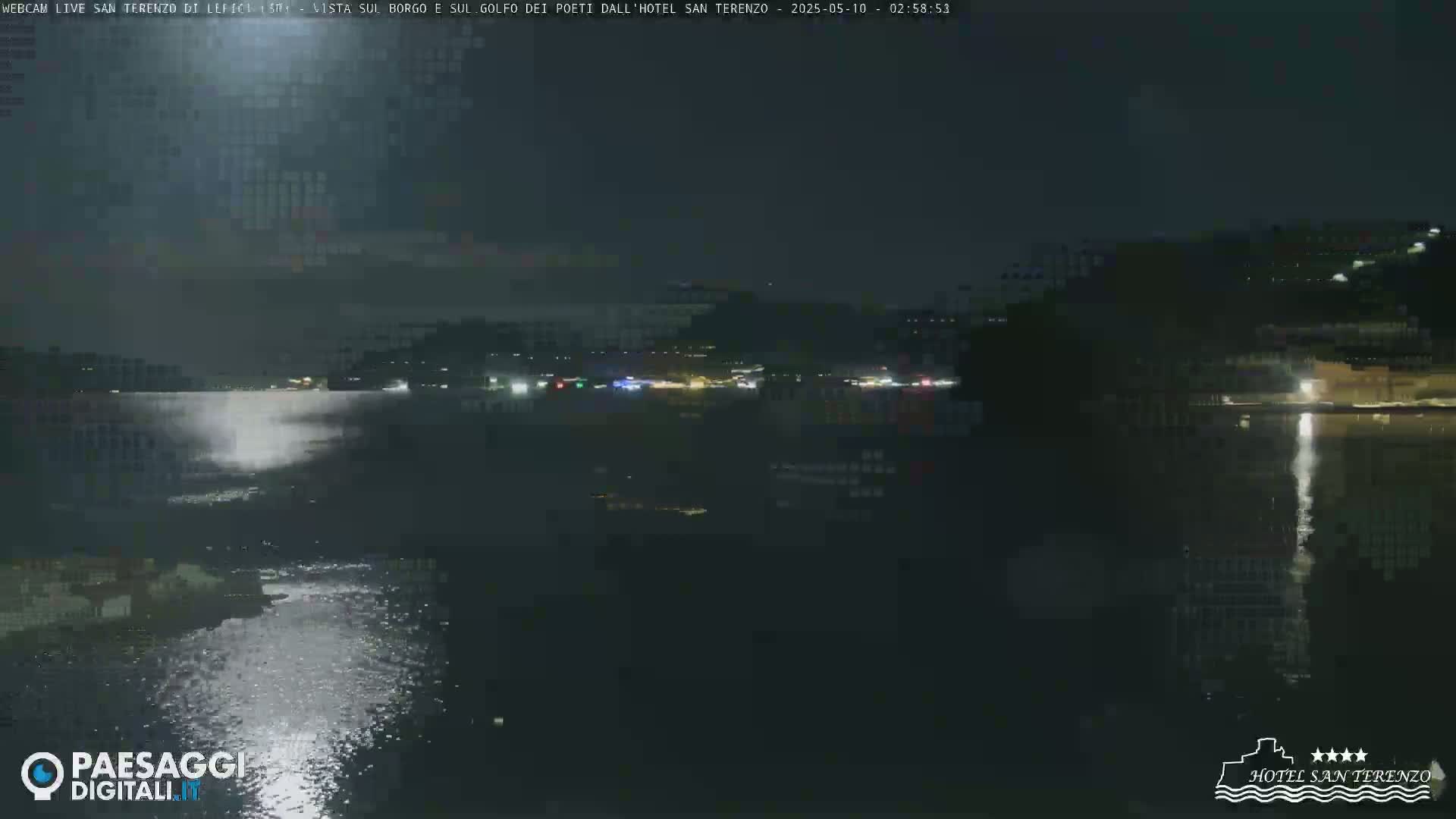 A nighttime view of a calm body of water reflecting lights from a town across the water under a dark sky.