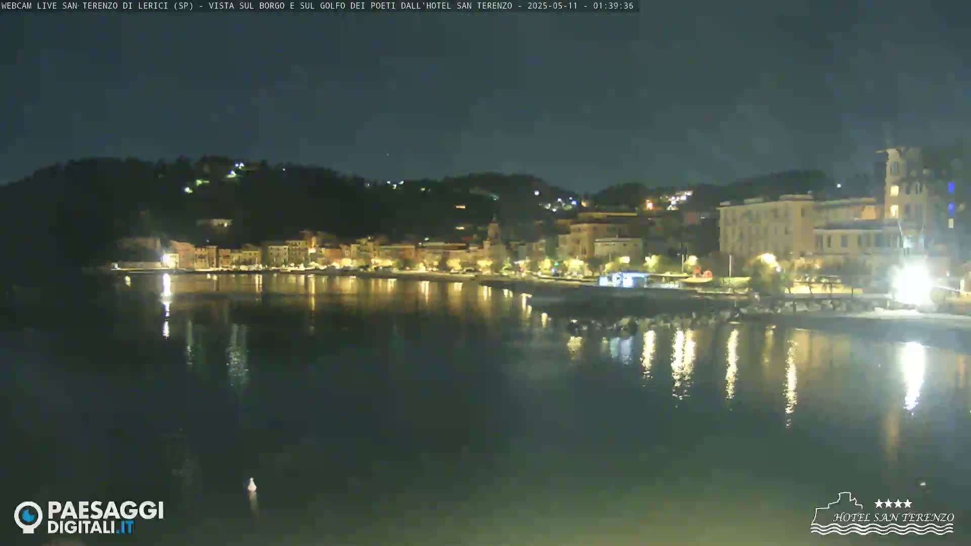 A nighttime view of a calm body of water reflecting the lights of a town nestled on a hillside.