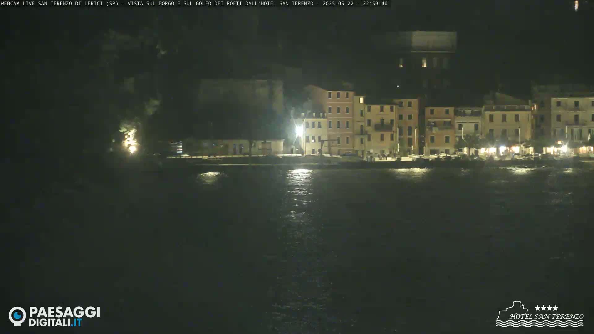 At night, a waterfront town with illuminated buildings is seen across a dark body of water.