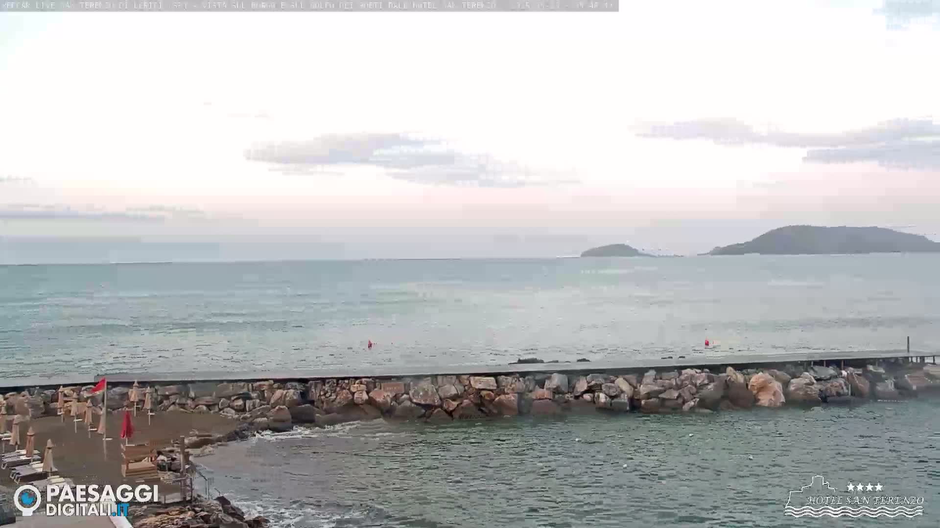 A rocky breakwater extends into a calm sea under an overcast sky, with islands visible in the distance.