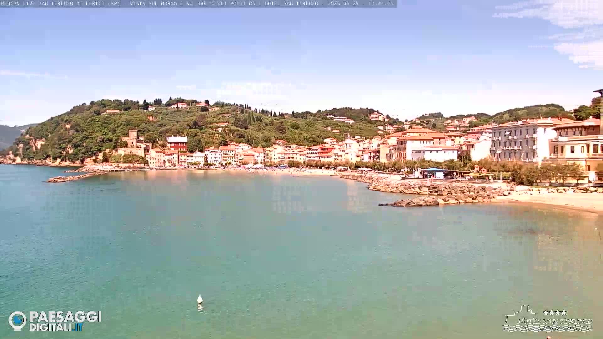 A picturesque coastal town nestled on a hillside, with a sandy beach and calm, clear water under a sunny sky.