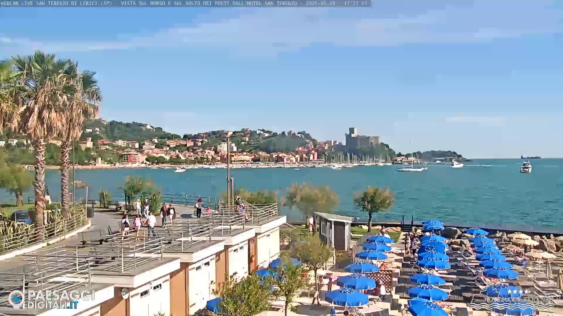 A sunny day at a beachside resort overlooking a calm bay with numerous boats and a town nestled on a hillside in the distance.