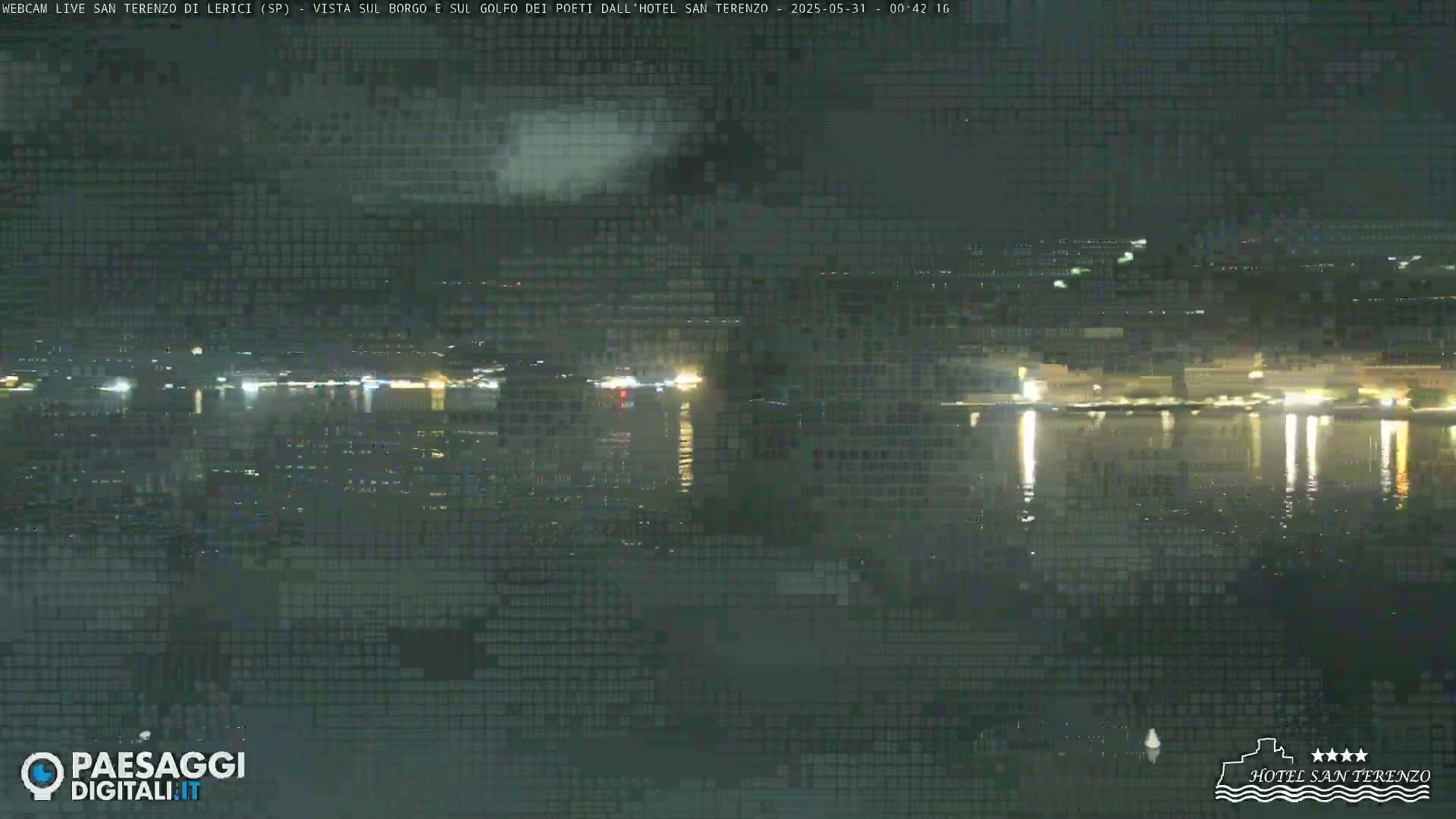 A nighttime view of a calm body of water reflecting the lights of a town across the water under a dark, mostly clear sky.