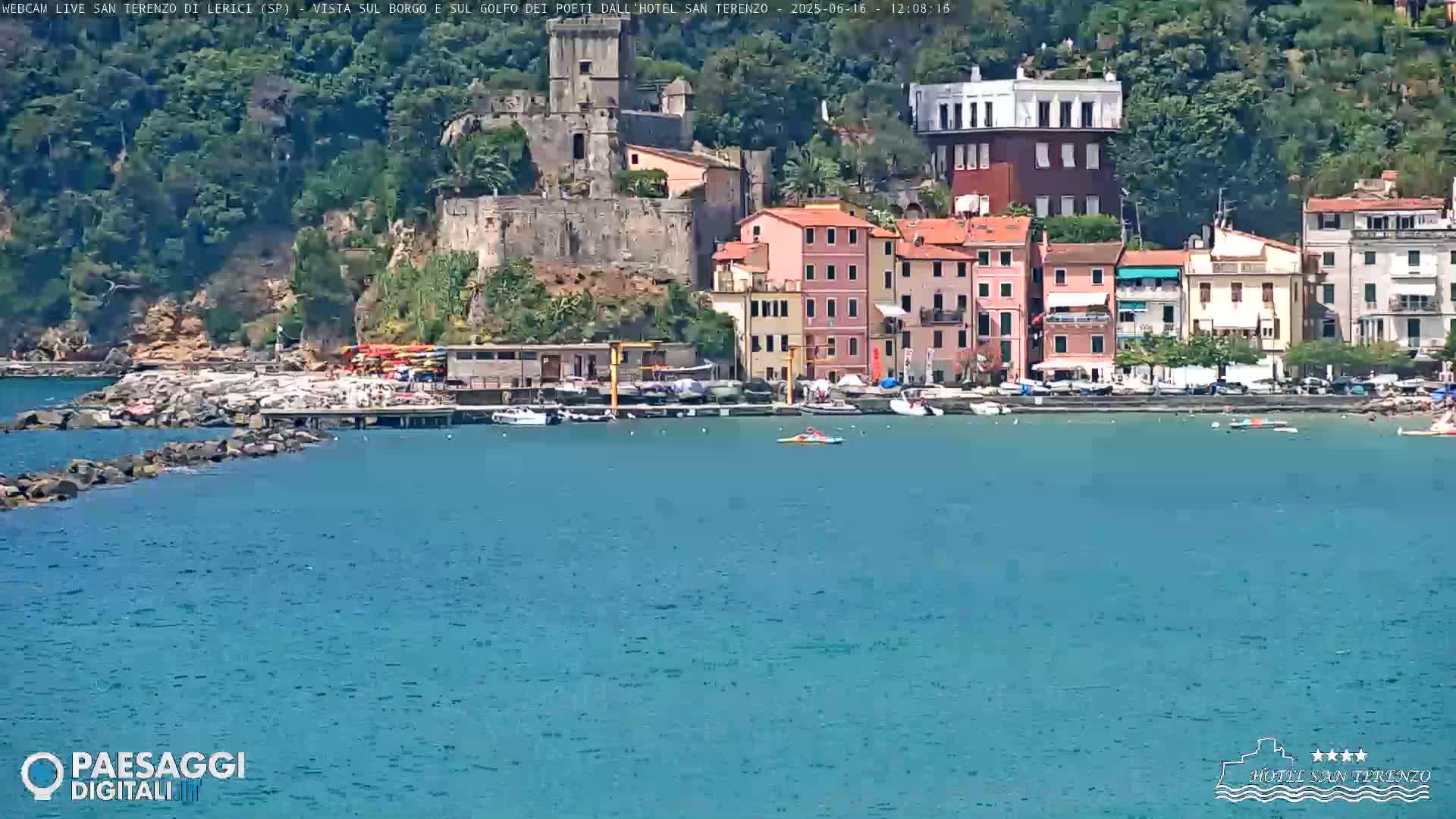 A picturesque waterfront town with colorful buildings and a stone fortress is visible across a calm, blue body of water on a sunny day.