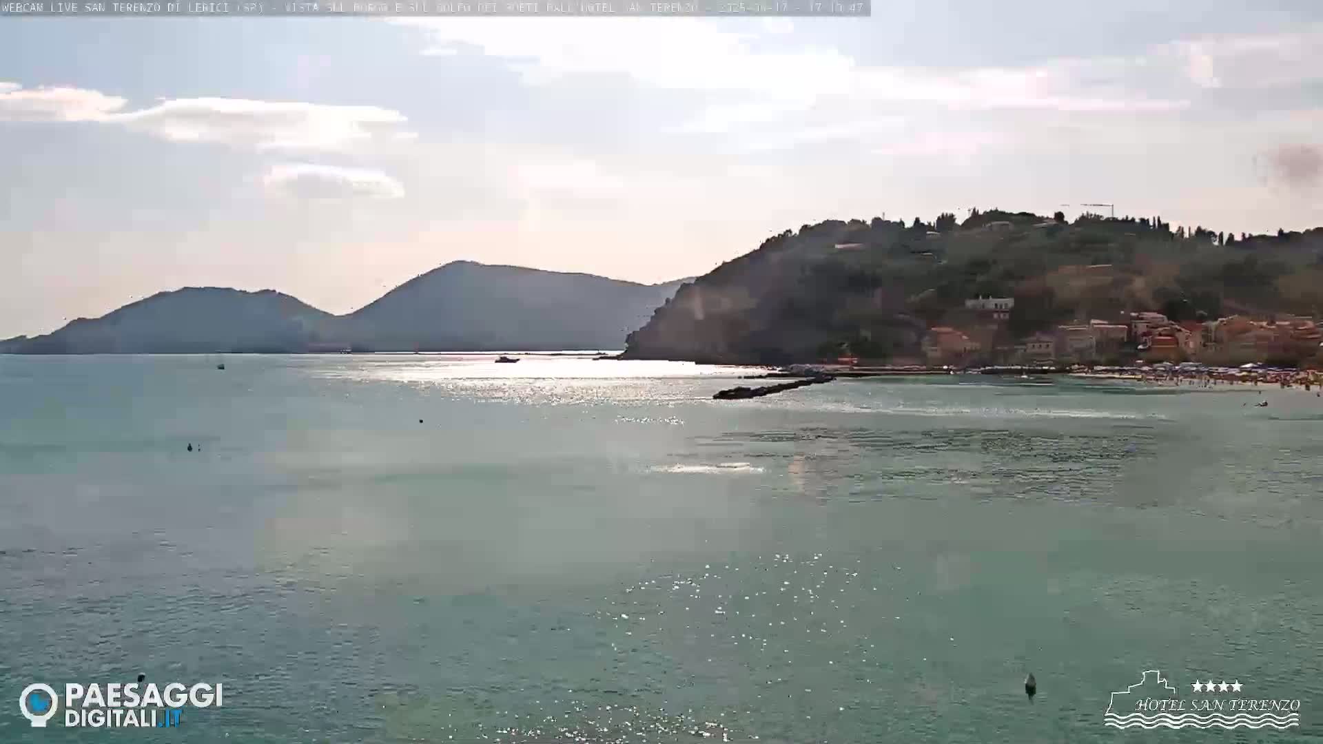 A sunny day shows a calm sea with a town and hills in the background.