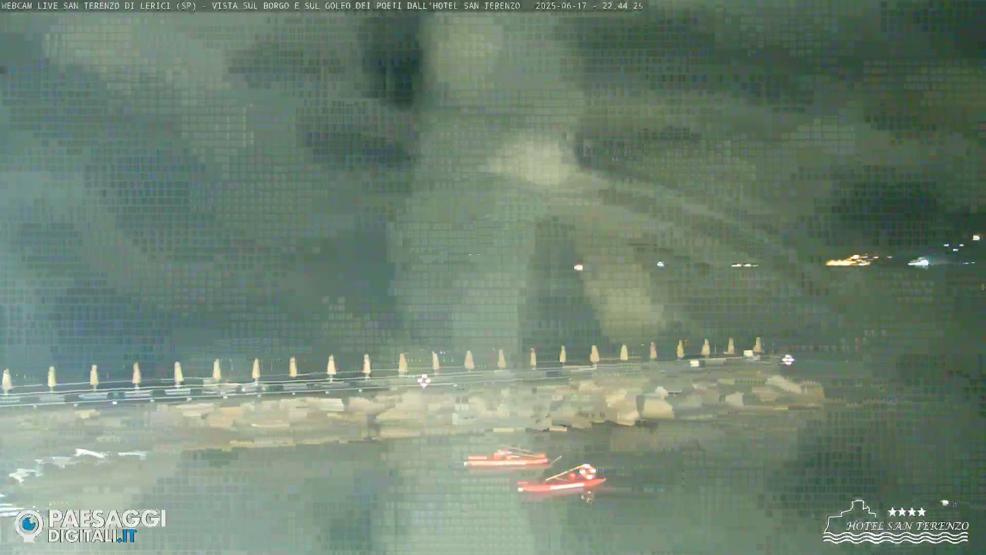 At night, two small red boats are in the water near a rocky shoreline with closed beach umbrellas.