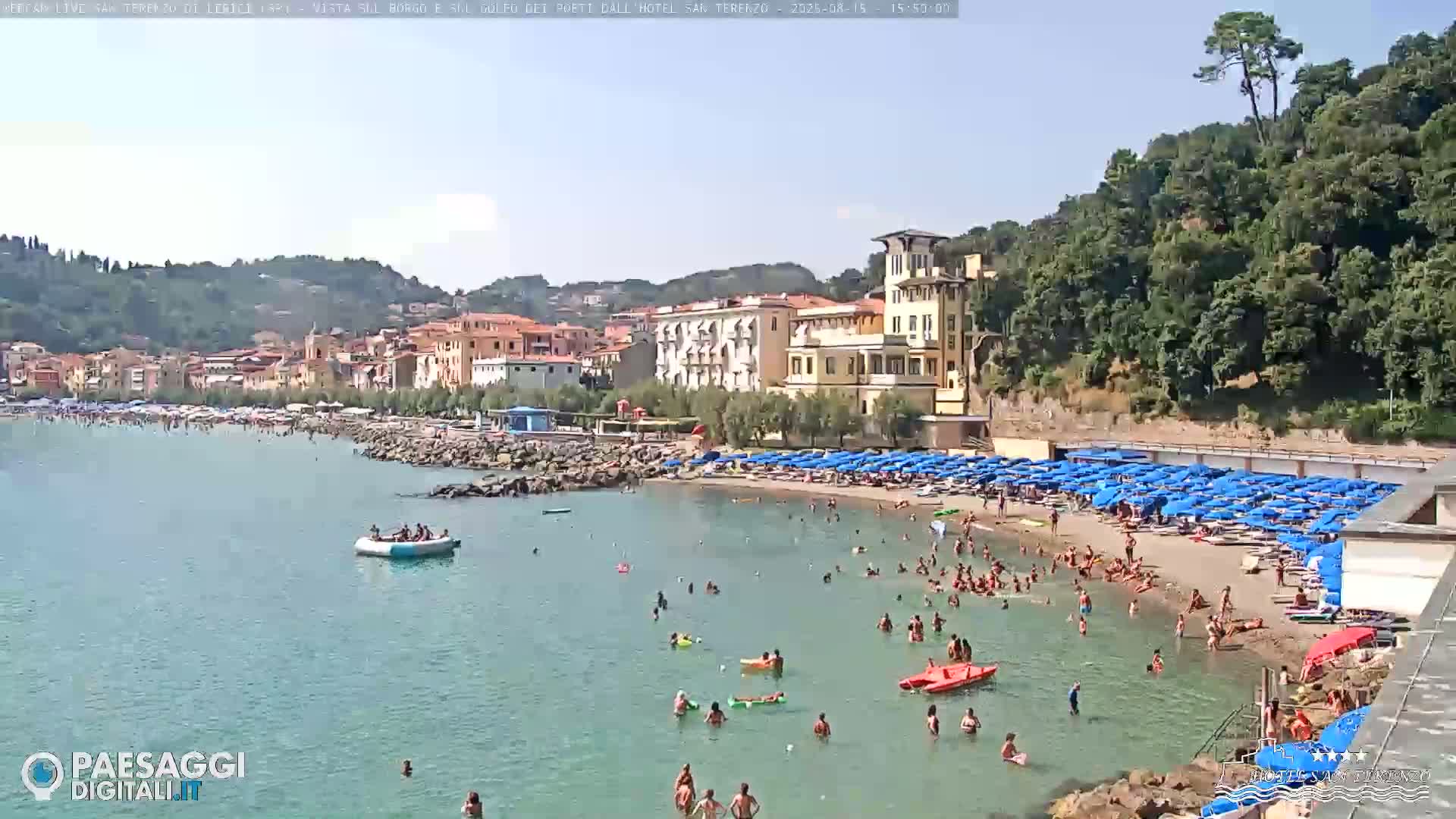A calm bay with a sandy beach and a town built on a hillside under a clear sky.