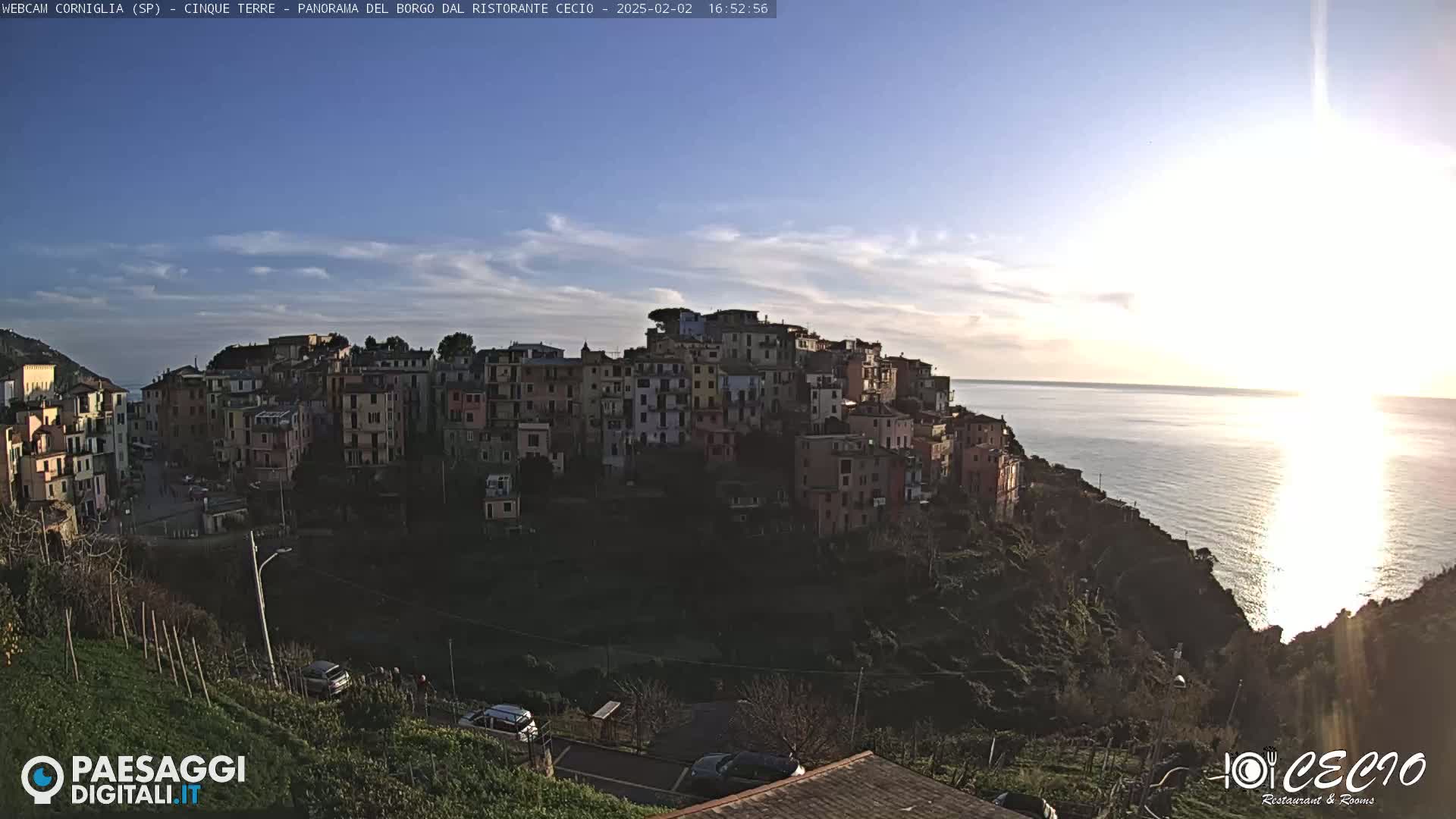 A colorful coastal village is perched on a cliff overlooking a calm sea under a mostly clear, bright sky.