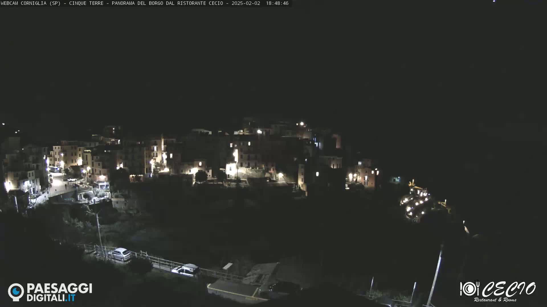 A nighttime, aerial view of a small, illuminated village nestled on a hillside.