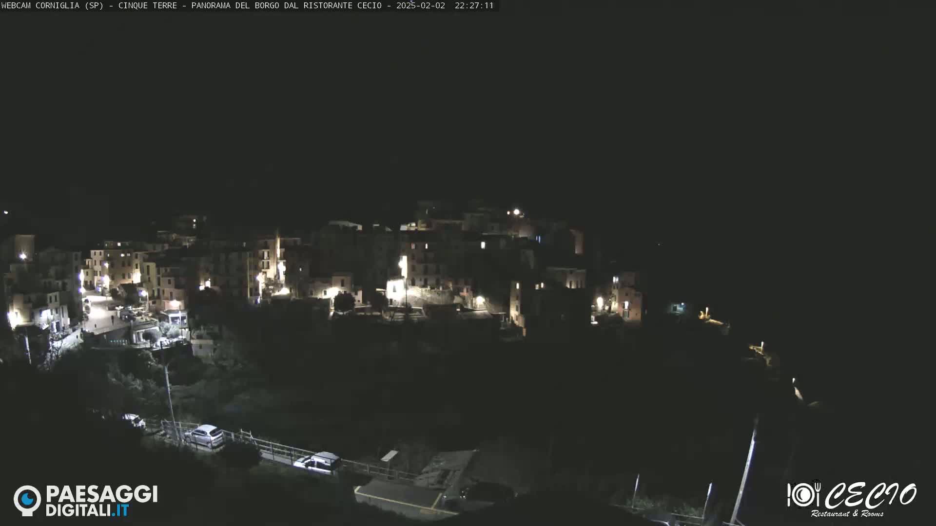 A nighttime, high-angle view shows a small, illuminated town nestled against a dark hillside.