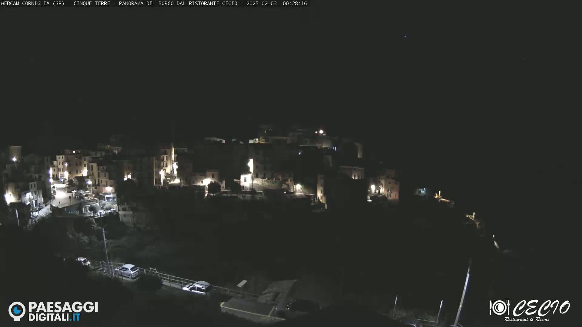 A nighttime, aerial view of a small, dimly lit town nestled on a hillside under a clear, dark sky.
