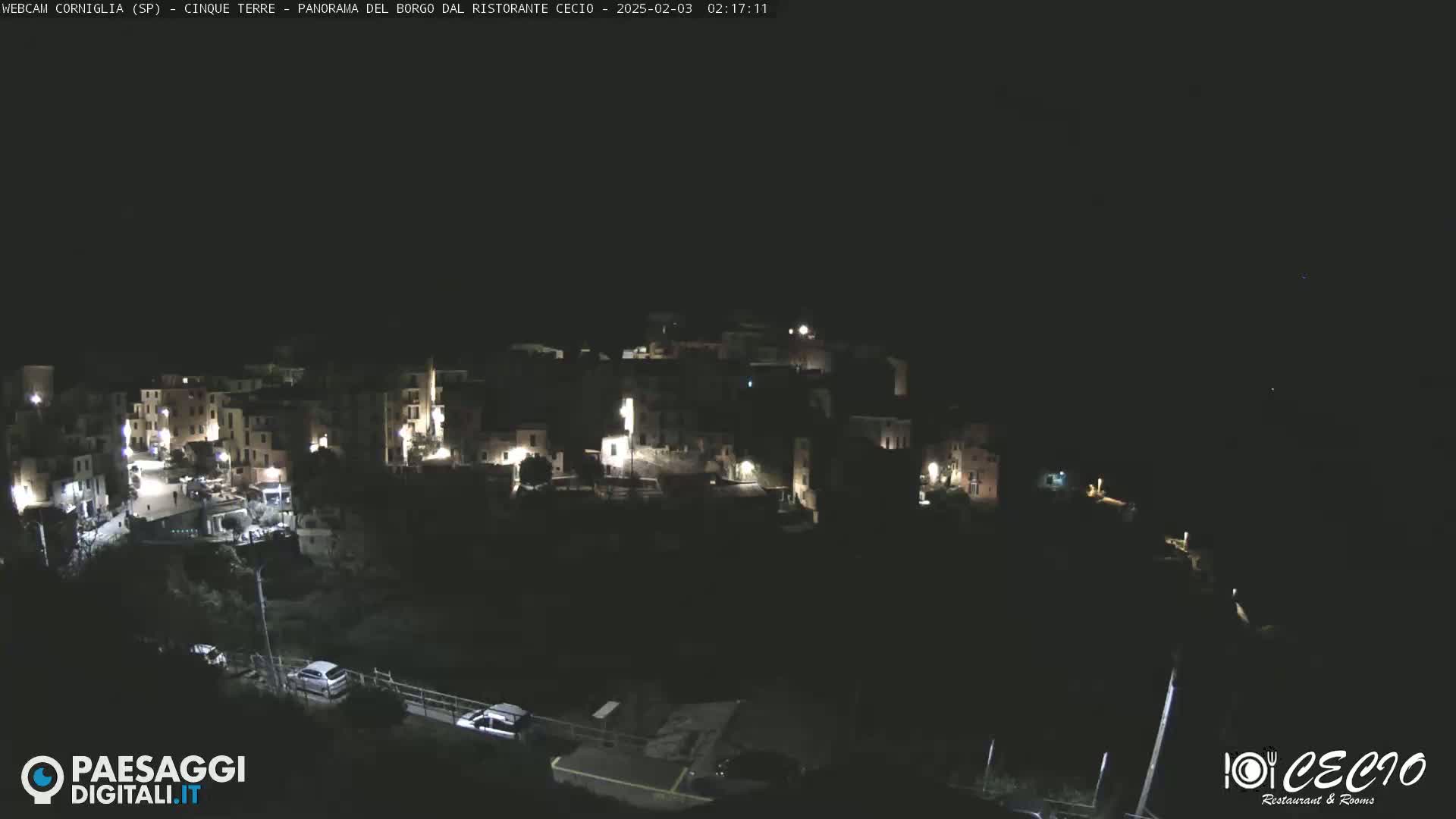 A nighttime, aerial view shows a small, dimly lit town nestled on a hillside.