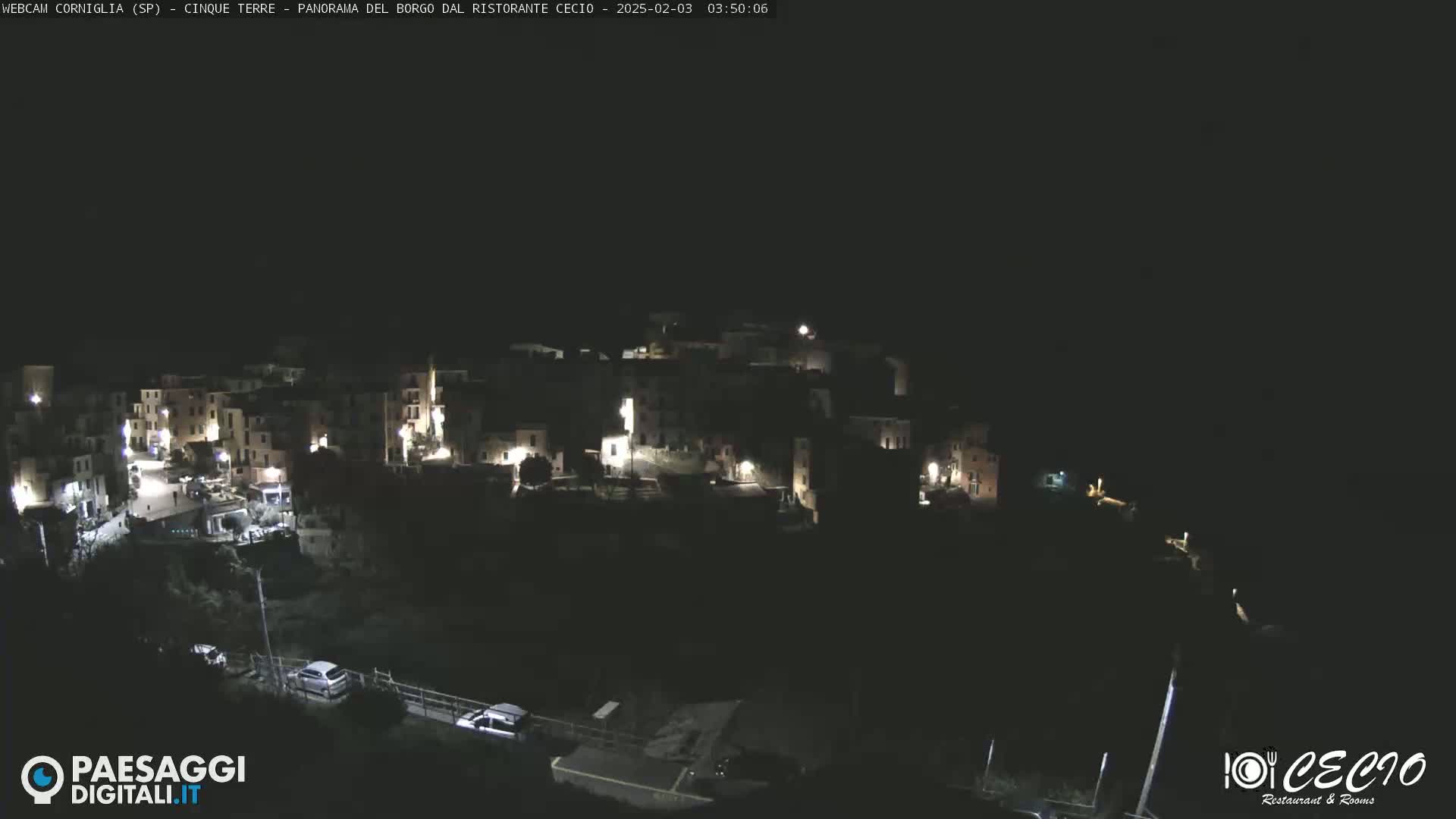 A nighttime, overhead view shows a small, dimly lit town nestled on a hillside.