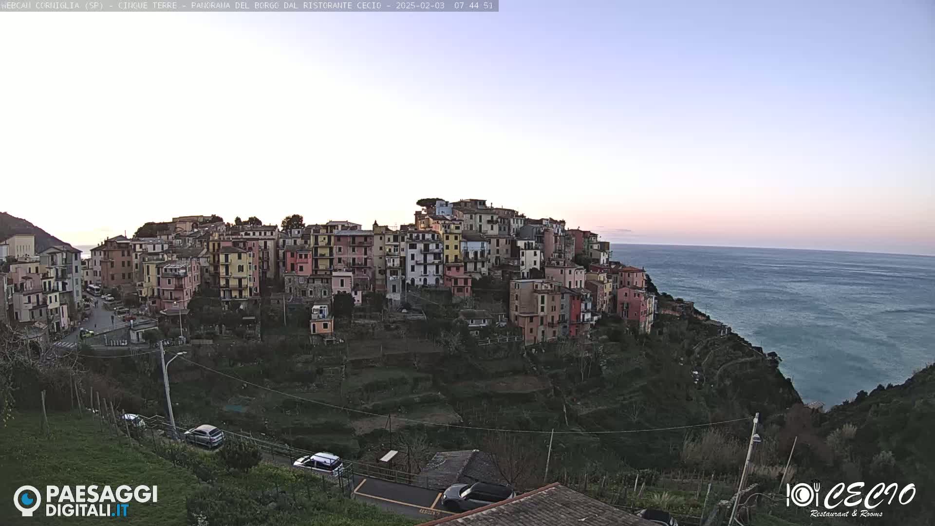 A colorful hillside village overlooks a calm, twilight ocean.