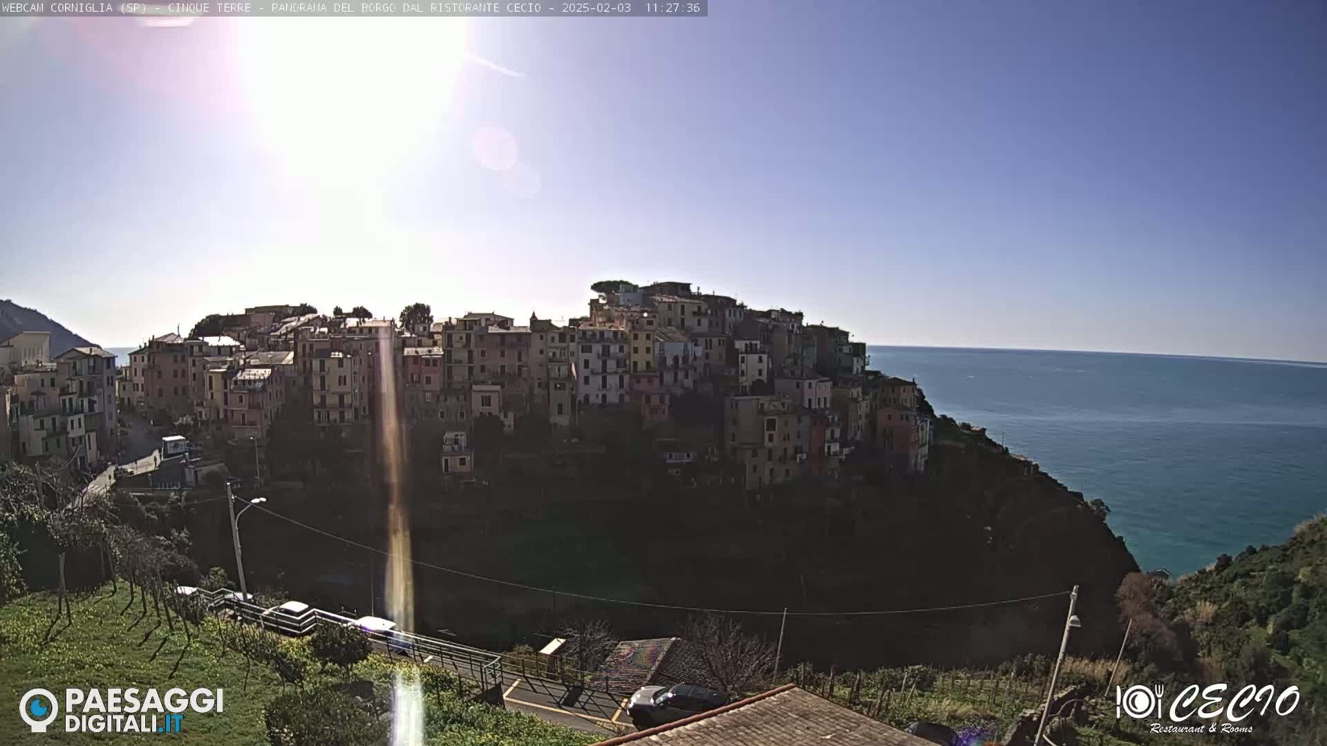 A hillside village of colorful buildings overlooks a calm blue ocean under a clear, sunny sky.