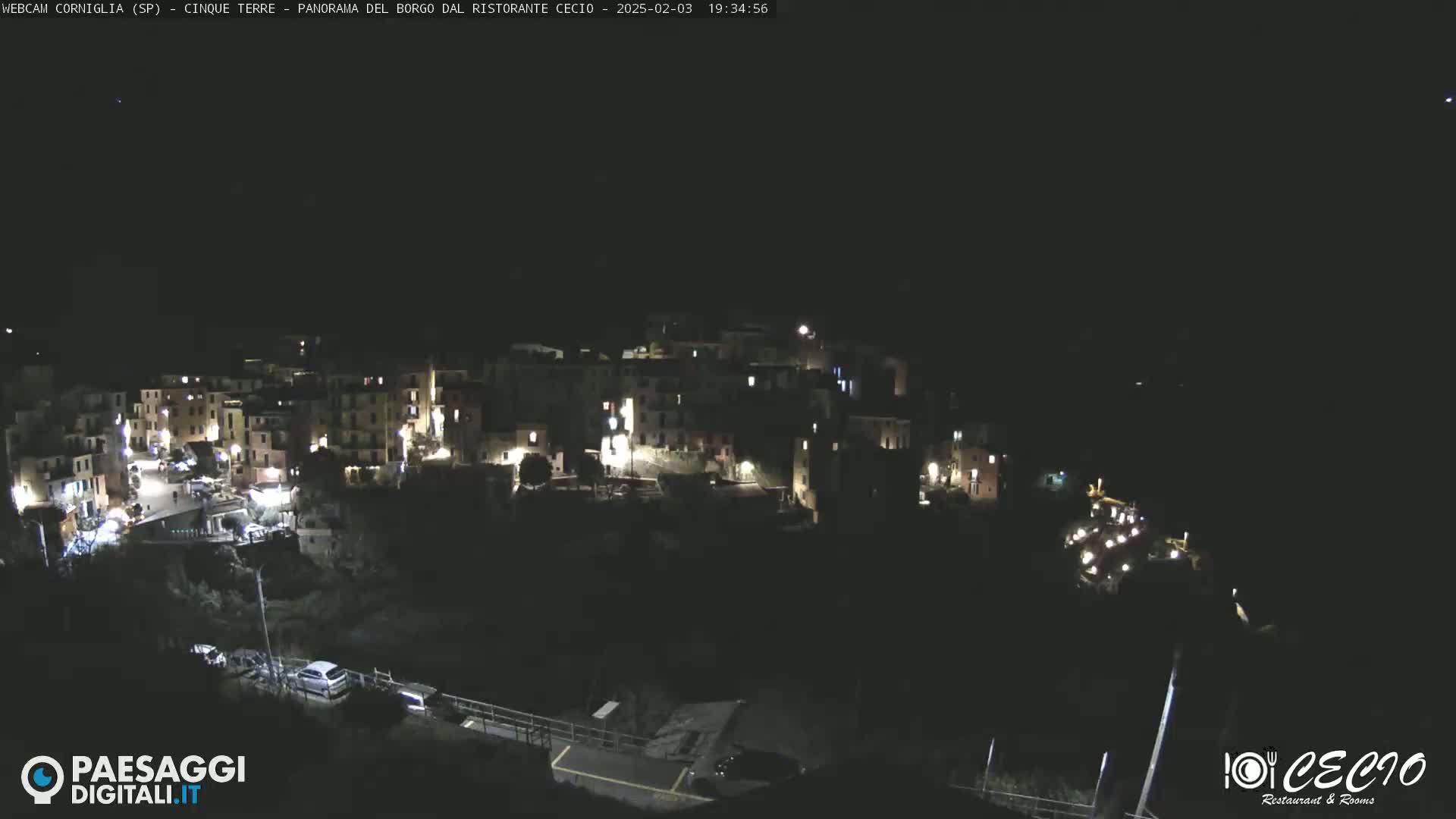A nighttime, high-angle view of a small, brightly lit town nestled into a dark hillside.