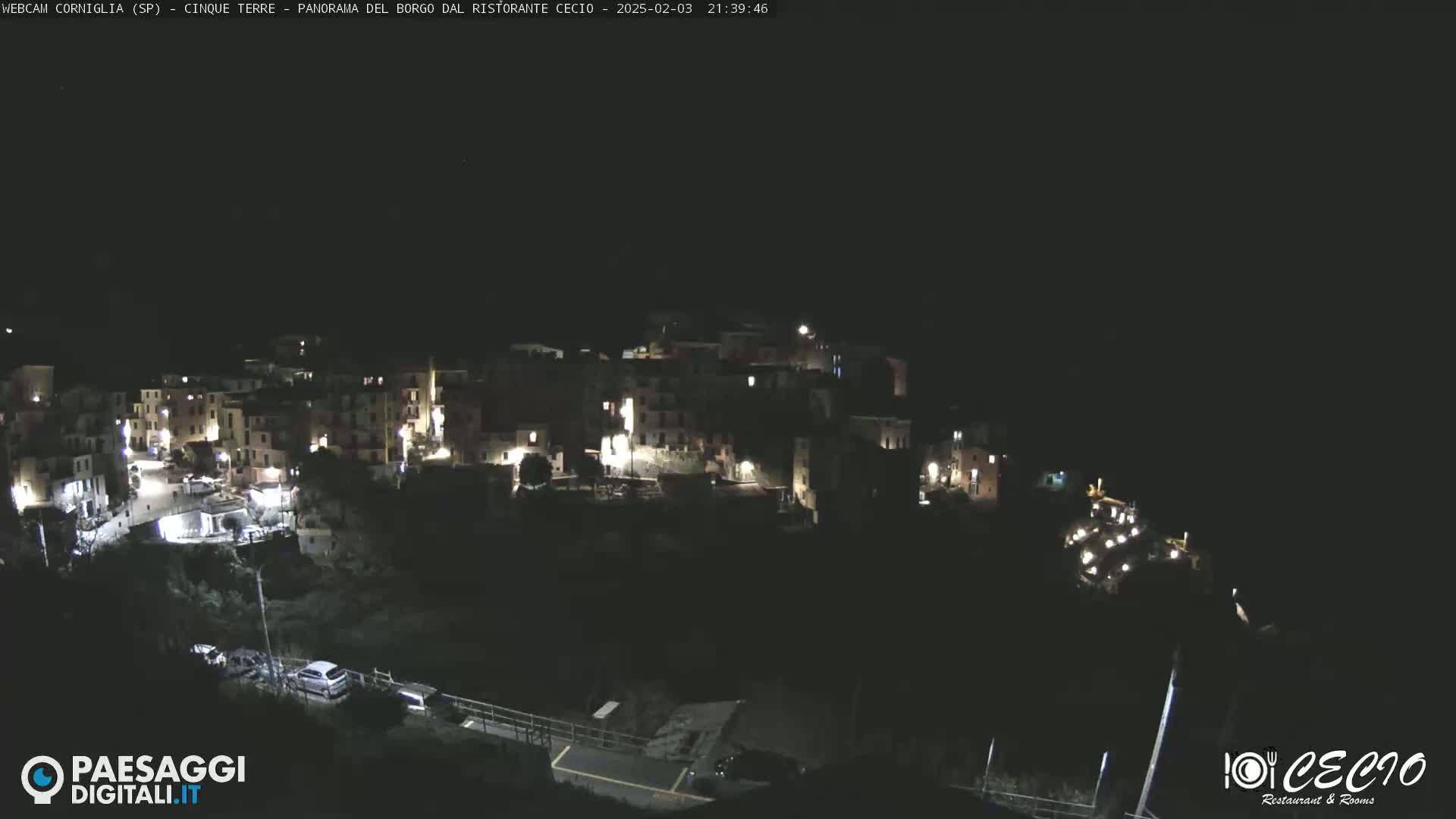 A nighttime view of a small, illuminated village nestled on a hillside under a clear, dark sky.