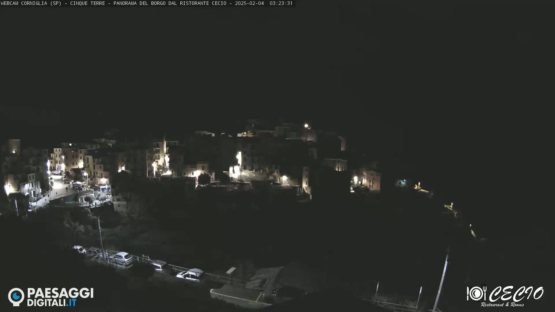 A nighttime, aerial view of a small, illuminated town nestled on a hillside under a clear, dark sky.
