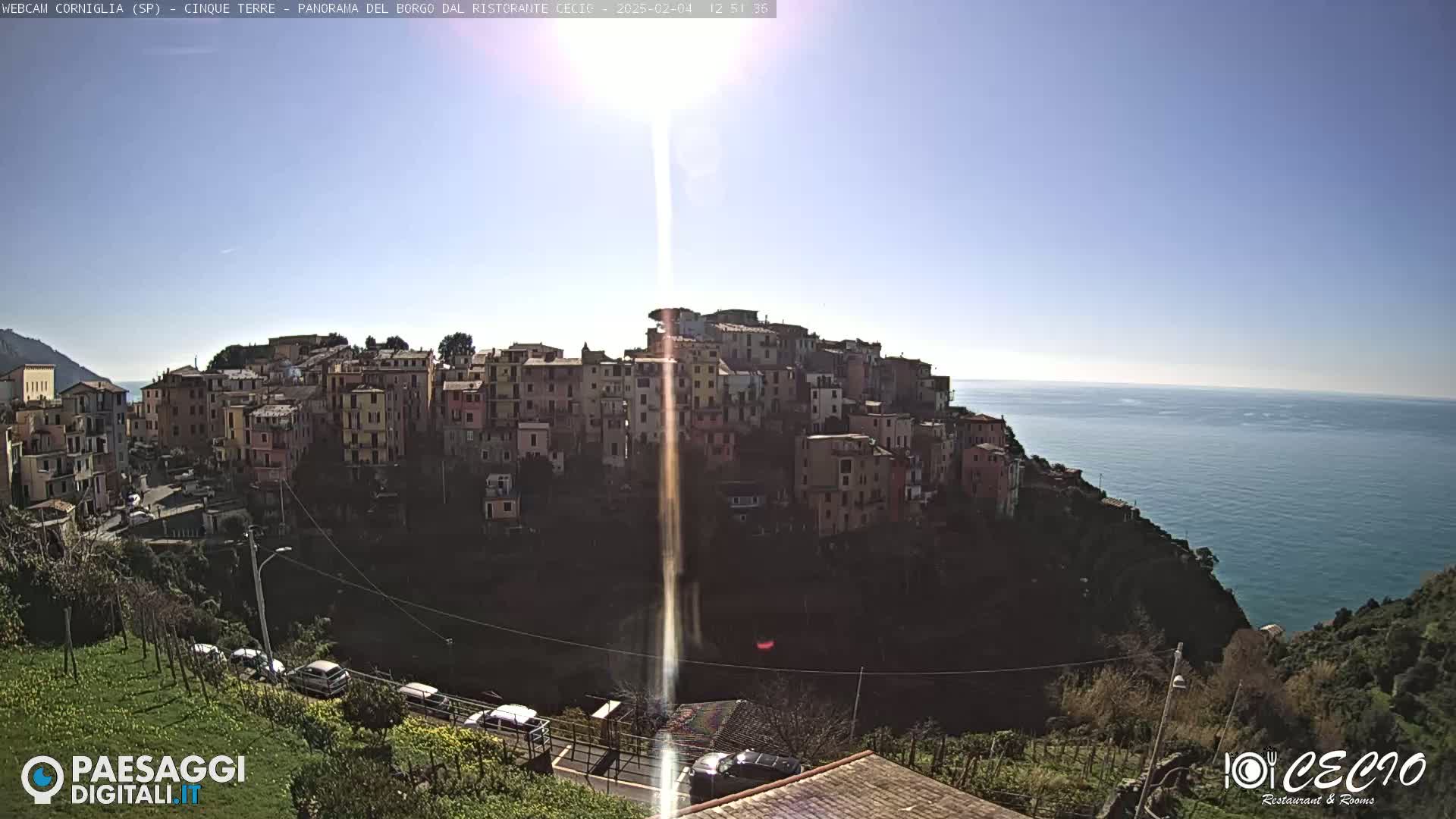 A sunny day shows a hillside village of colorful buildings overlooking a calm ocean.