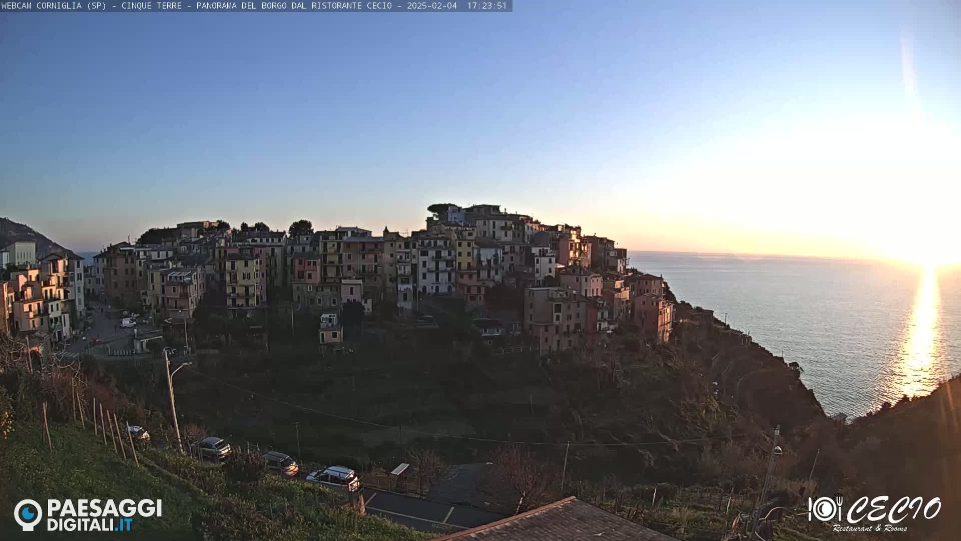 A colorful hillside village overlooks a calm sea at sunset.
