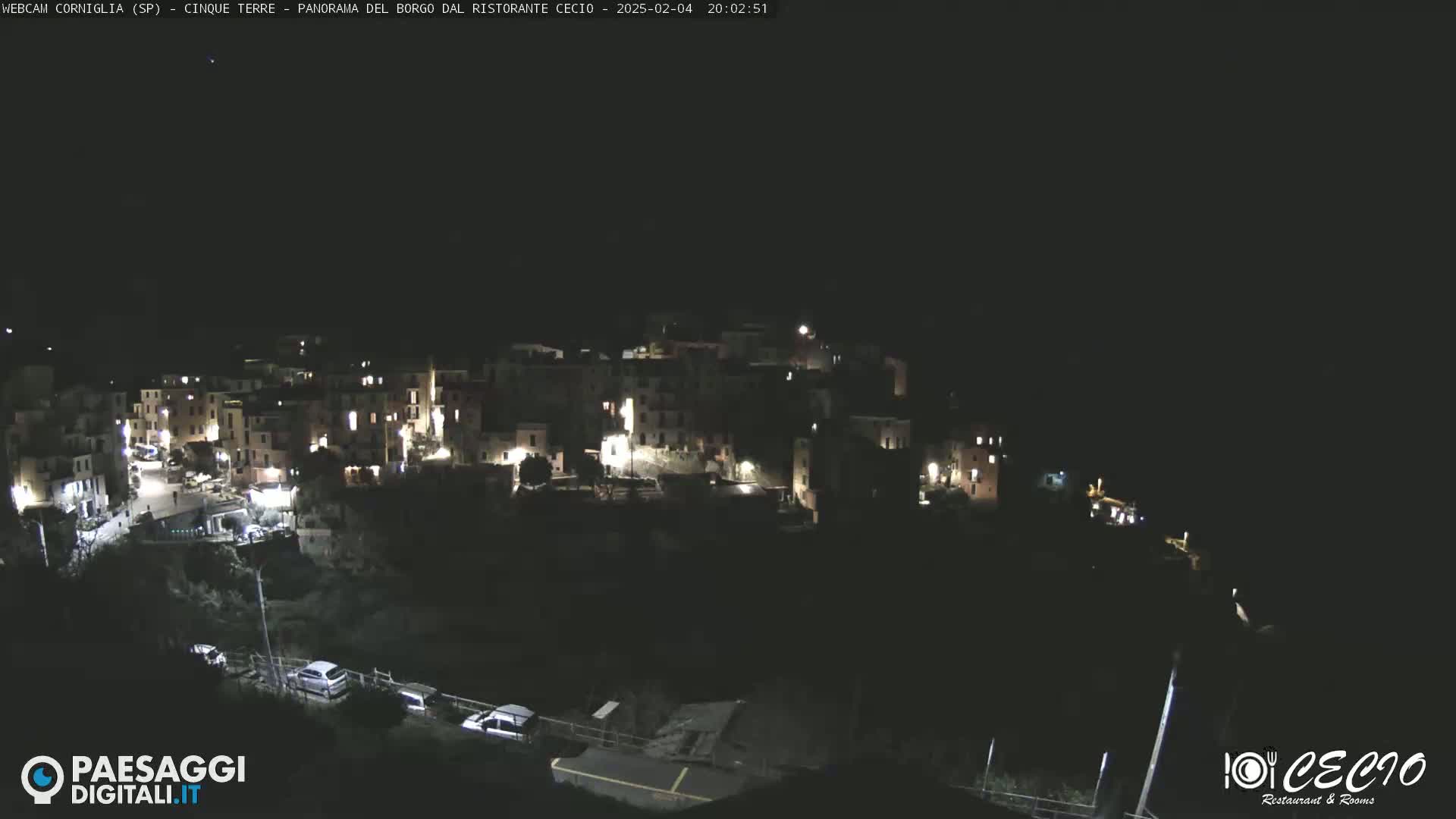 A nighttime, high-angle view of a small, illuminated village nestled on a dark hillside.