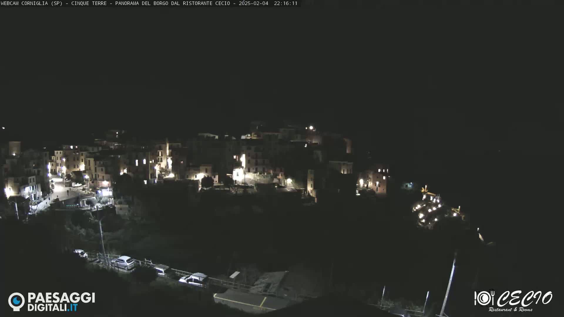 A nighttime view of a small, dimly lit town nestled on a hillside, under a clear, dark sky.