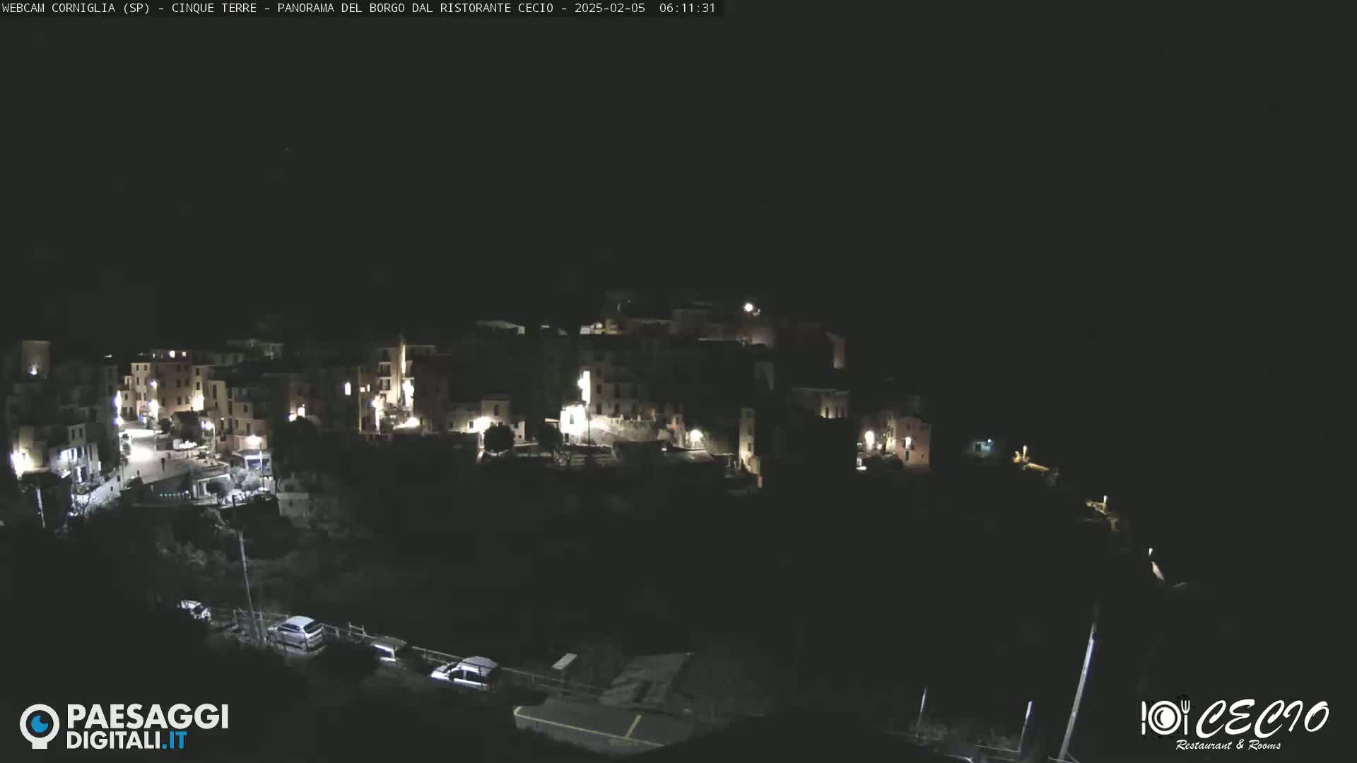 A nighttime, aerial view of a small, illuminated village nestled on a hillside under a dark sky.