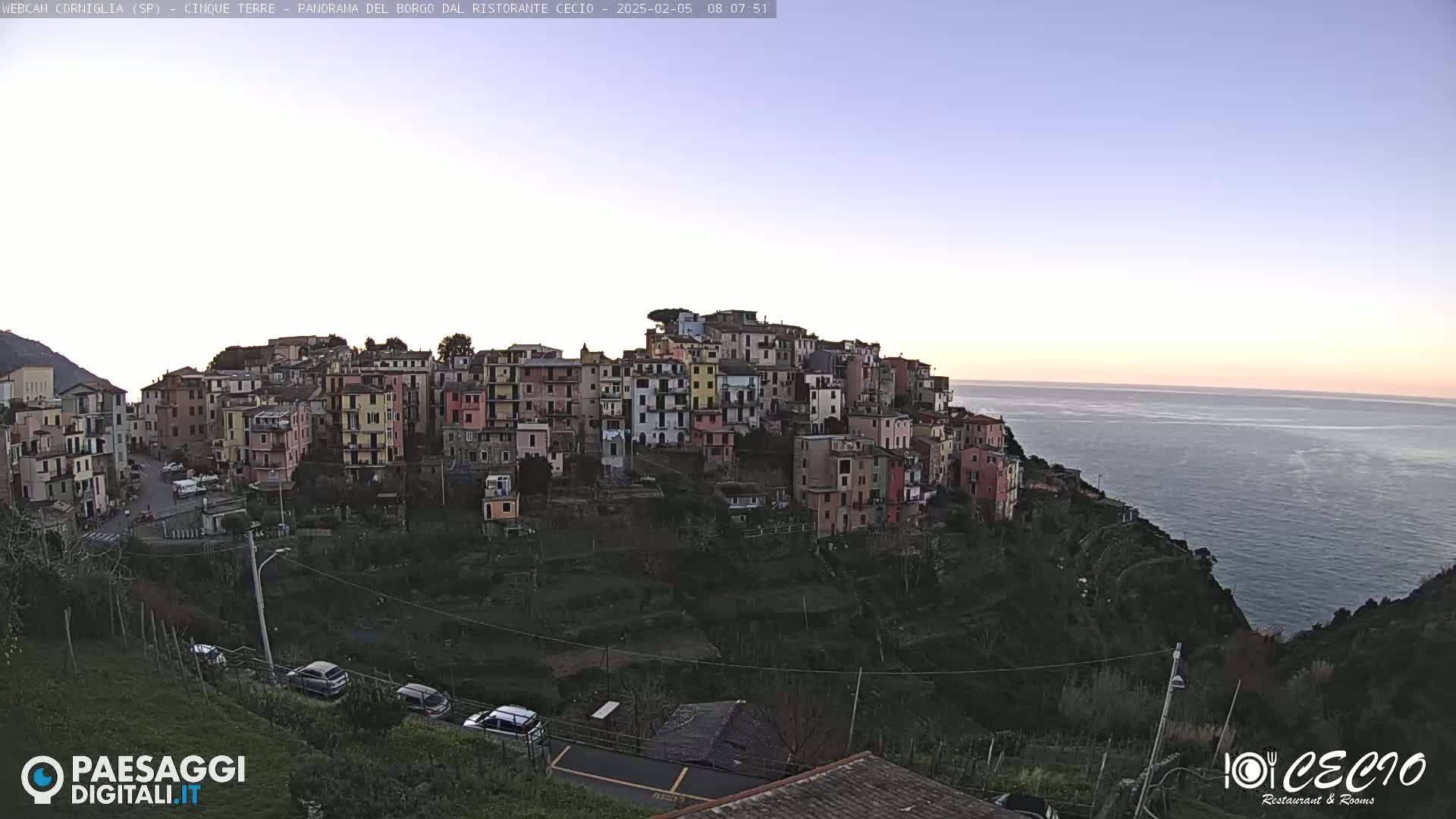 A coastal village of colorful buildings on a hillside overlooks a calm sea under a twilight sky.