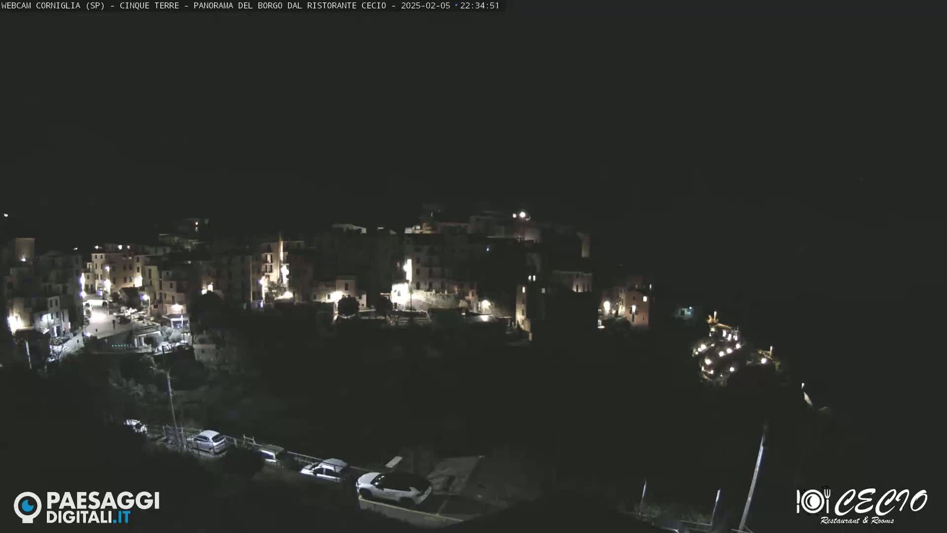 A nighttime view of a small, illuminated town nestled on a hillside under a dark sky.