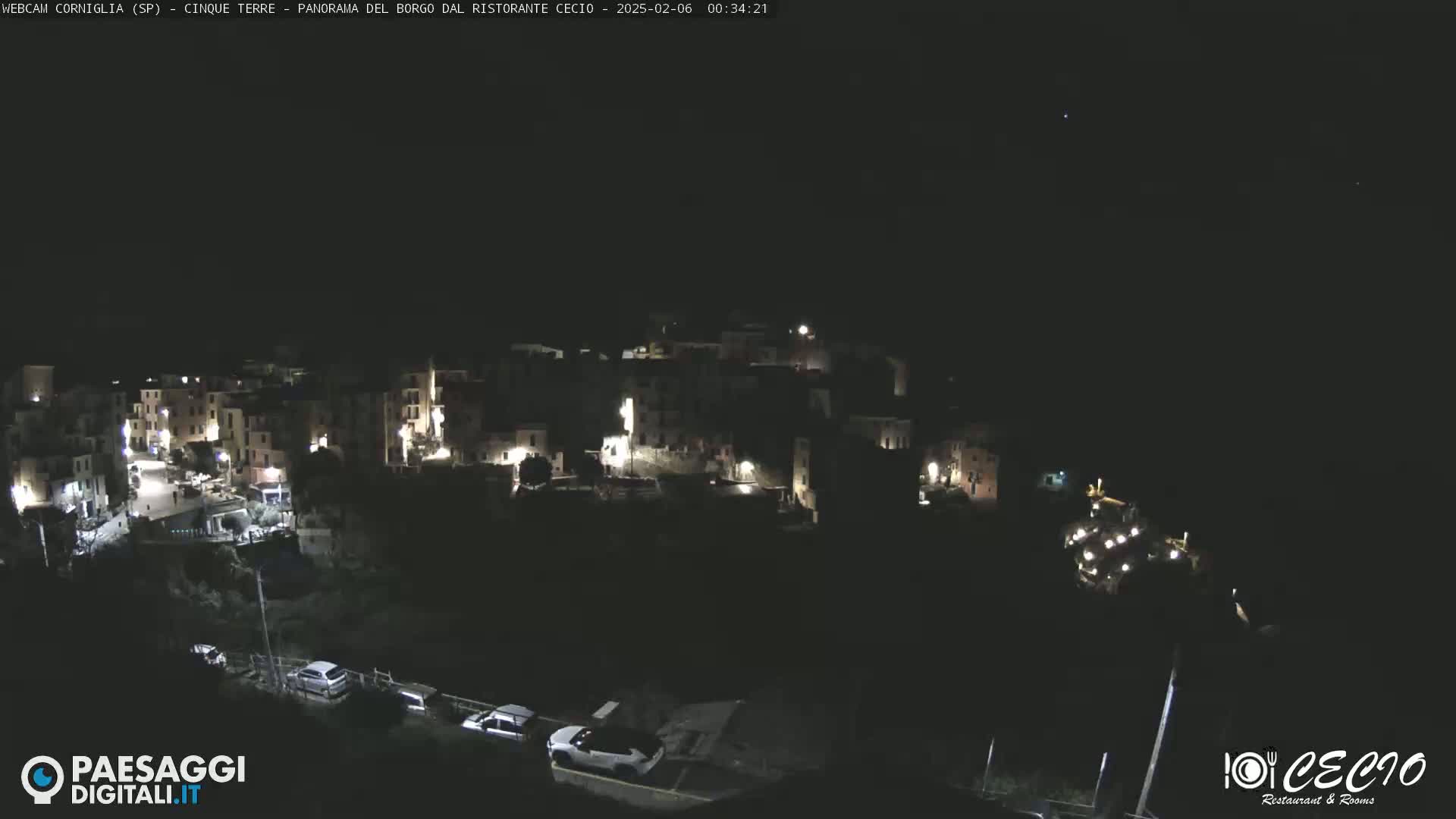 A nighttime, overhead view of a small, illuminated town nestled on a hillside under a clear, dark sky.