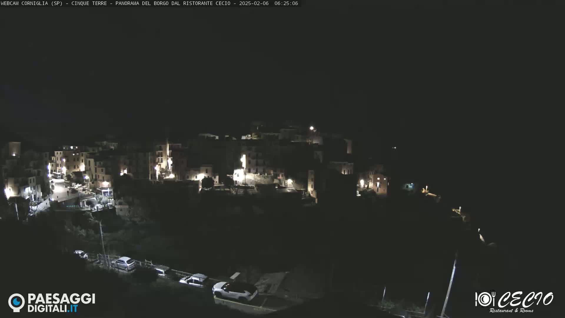 A nighttime, overhead view of a small, illuminated town nestled on a hillside.