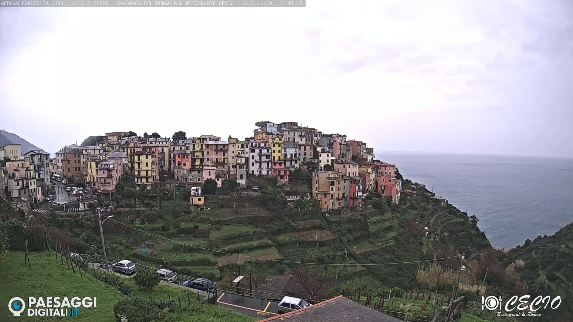 A colorful hillside village overlooks a calm sea under an overcast sky.
