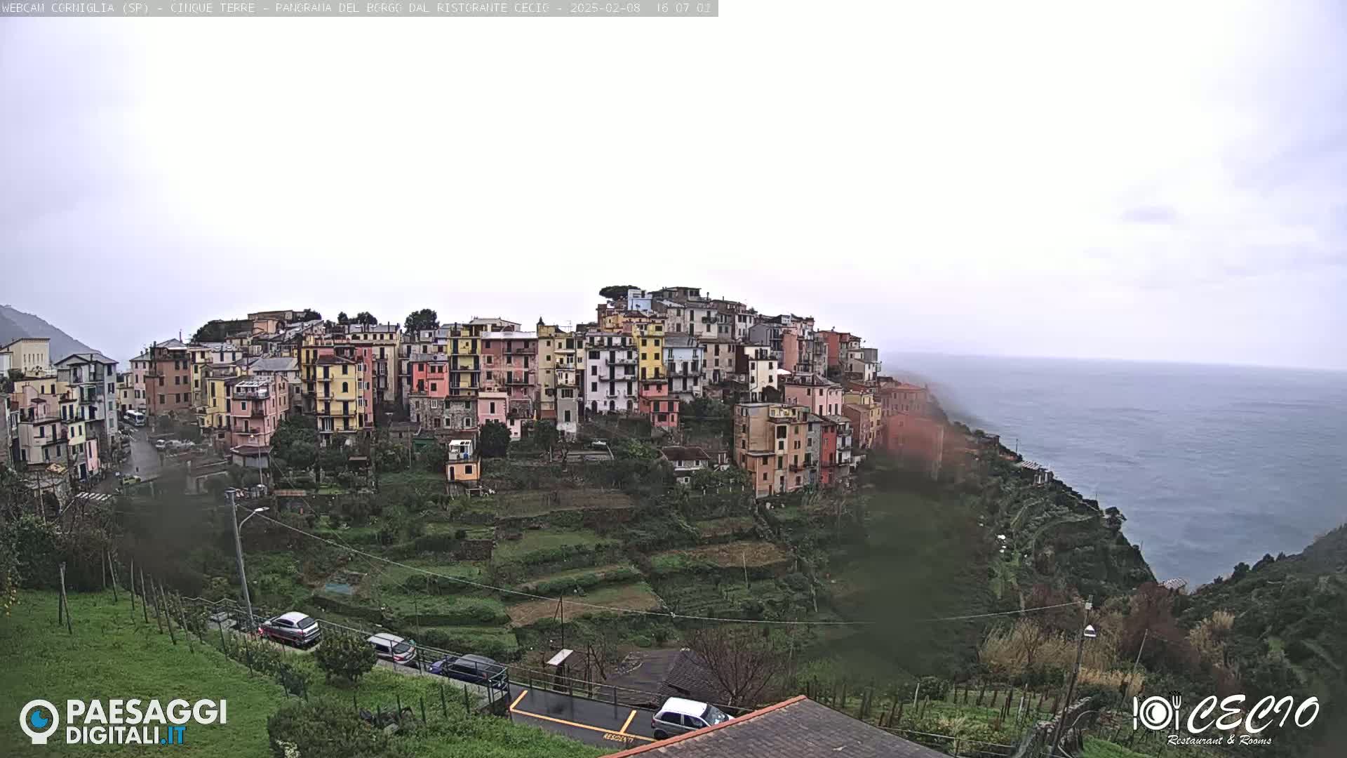 A hillside village of colorful buildings overlooks a calm ocean under an overcast sky.