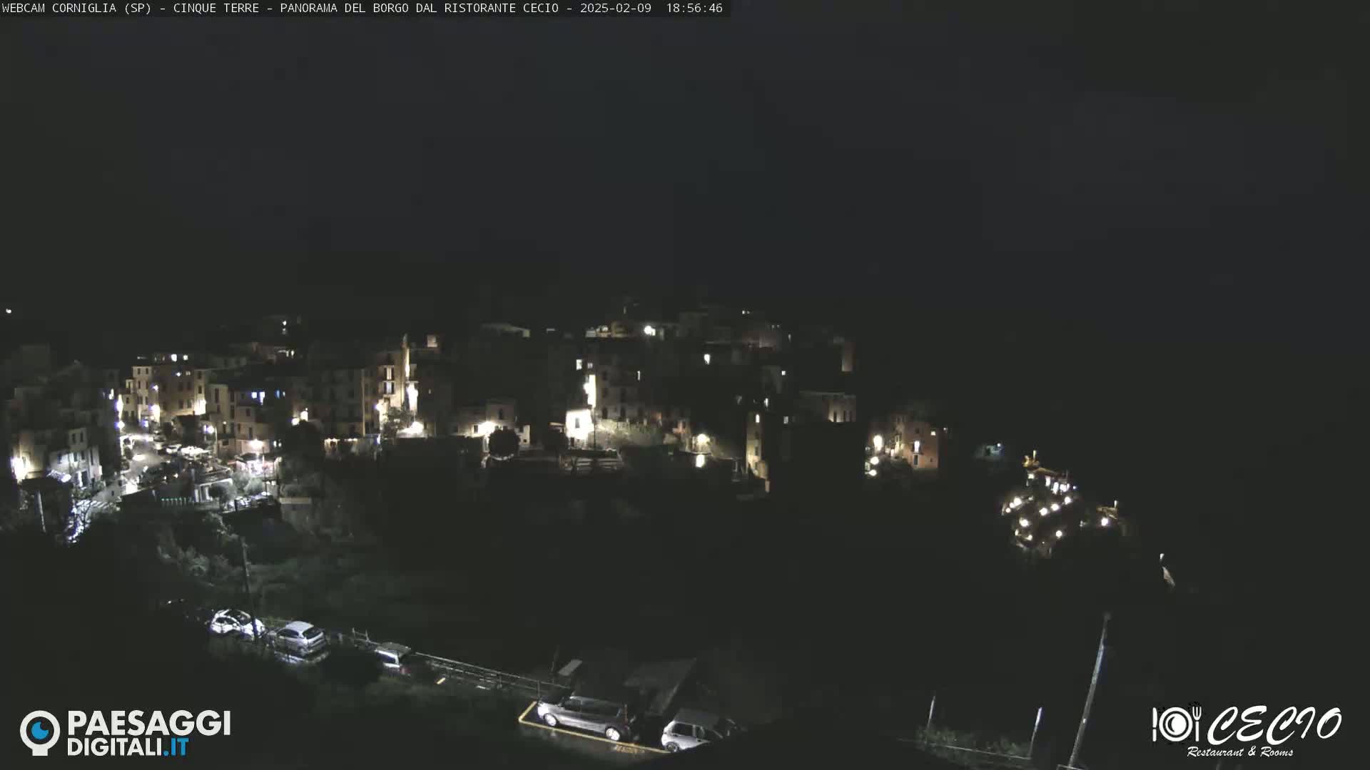 A nighttime, aerial view of a small, illuminated village nestled on a dark hillside.